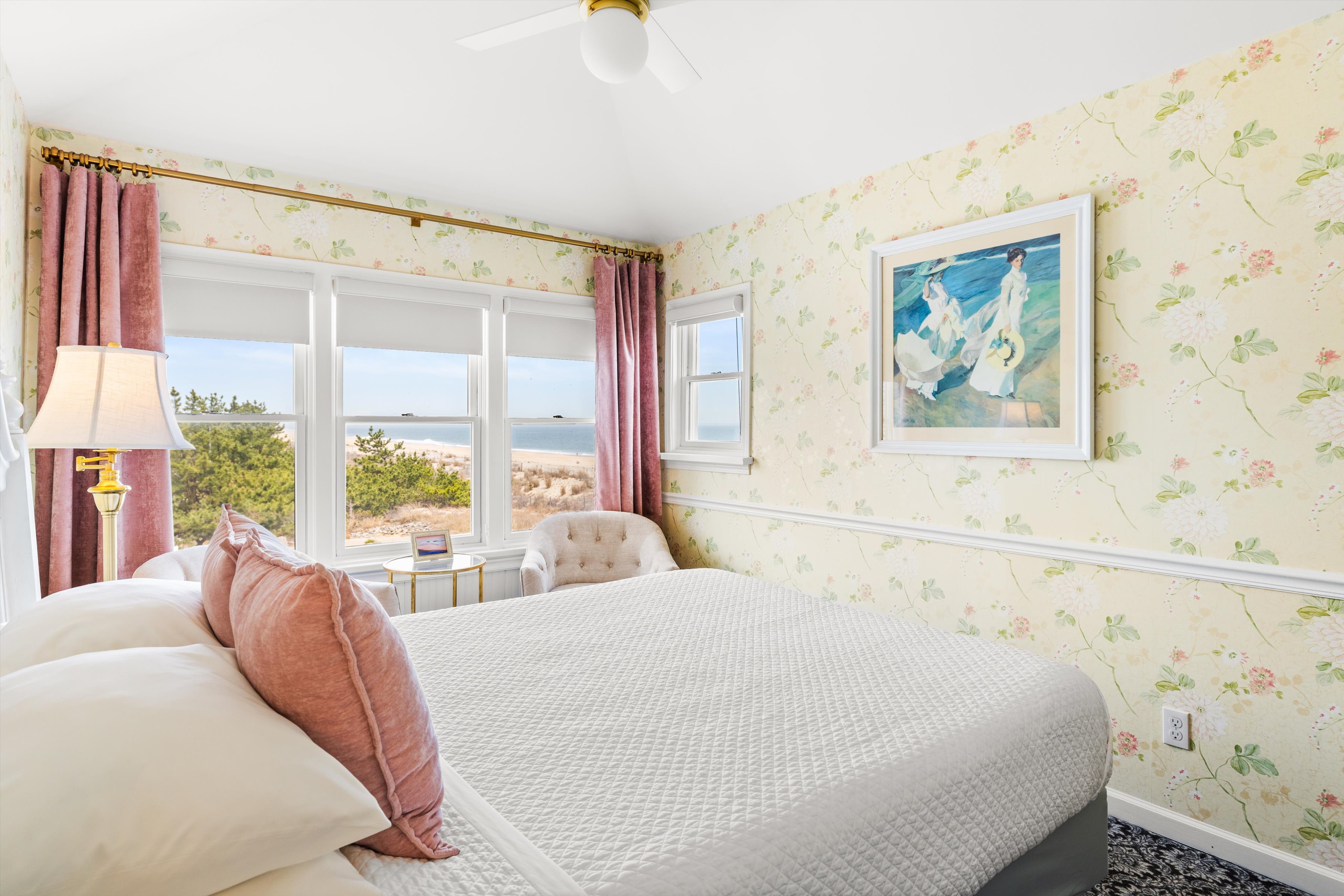 A cozy guest room with a large bed, floral wallpaper, and a view of the outdoors.