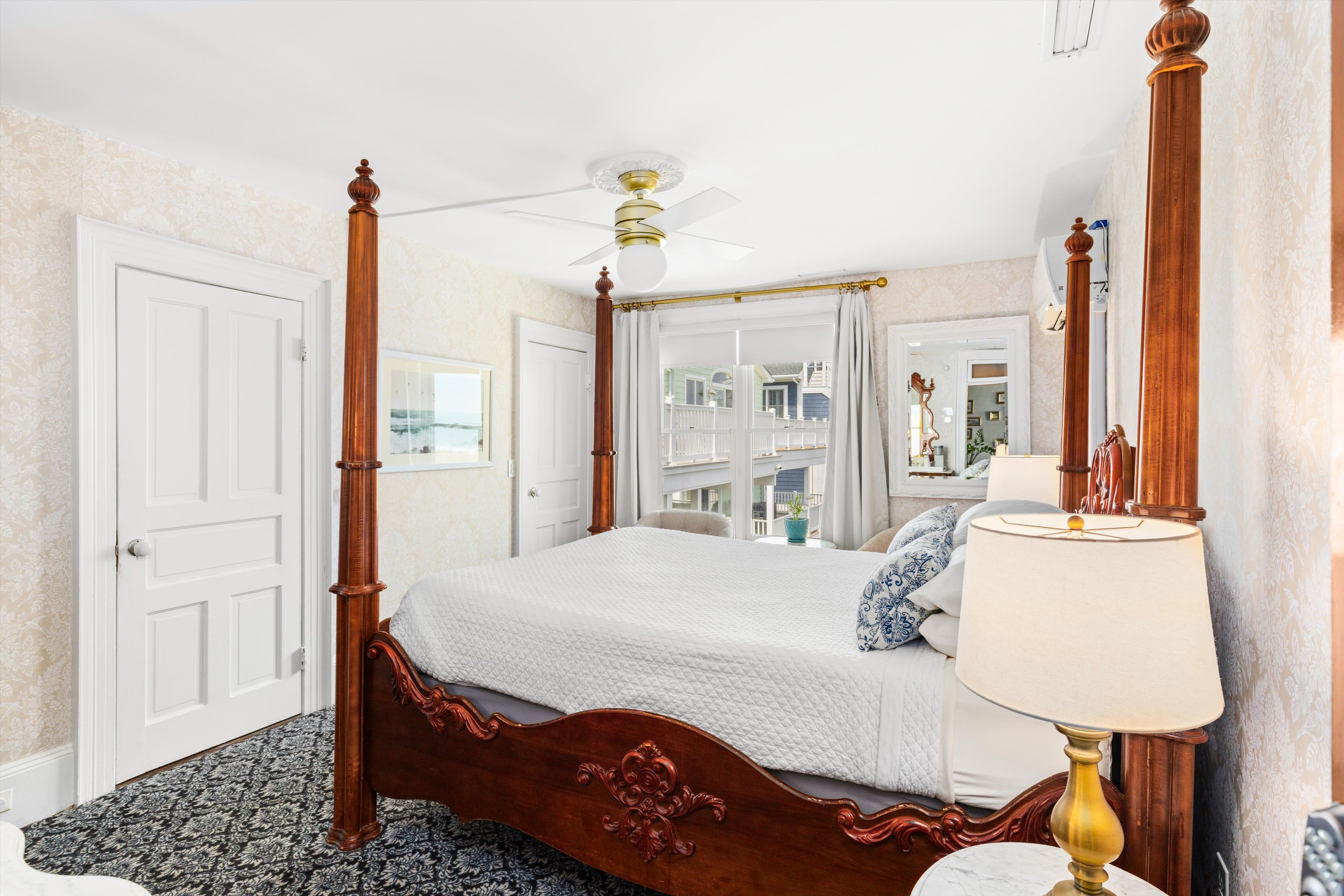 A wide view of a guest room with a four-poster bed, ceiling fan, and window with a view.