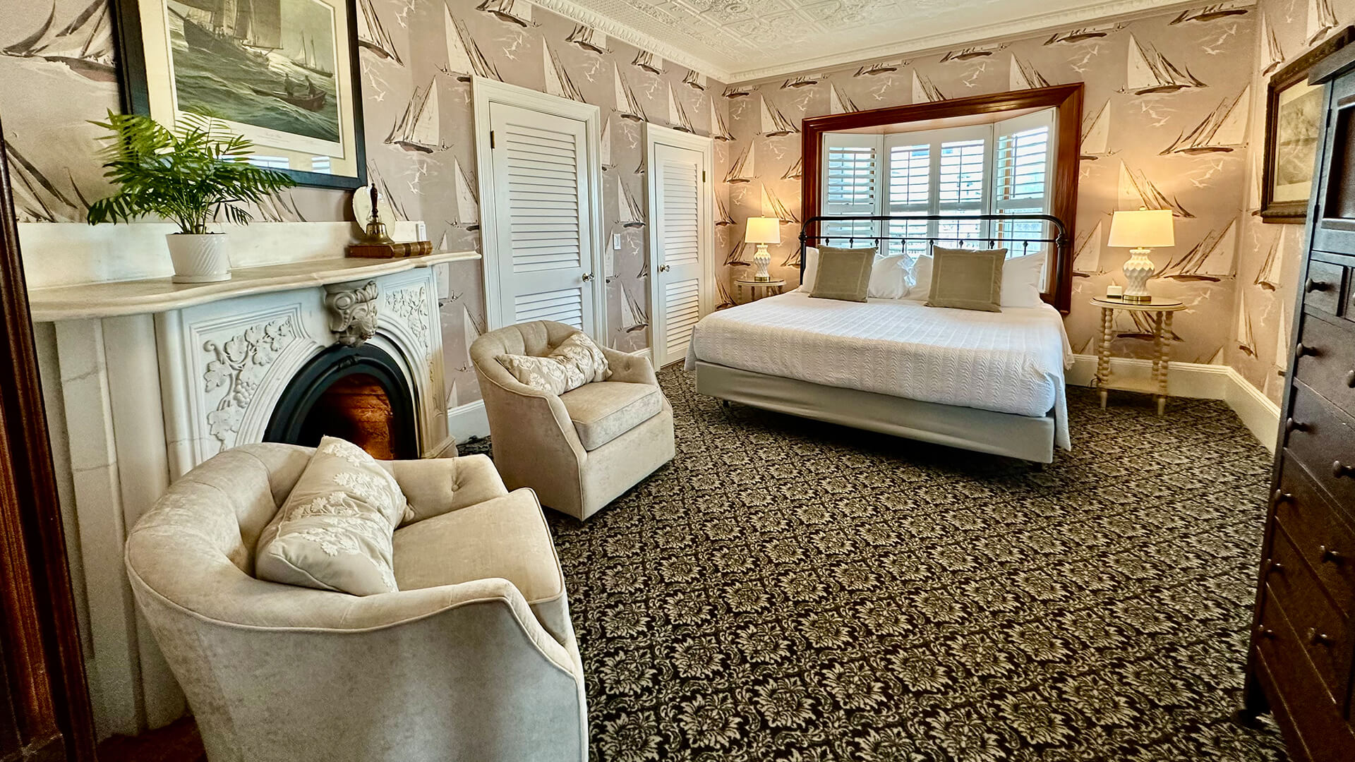 A wide view of a cozy guest room with a fireplace, bed, chair, and window.