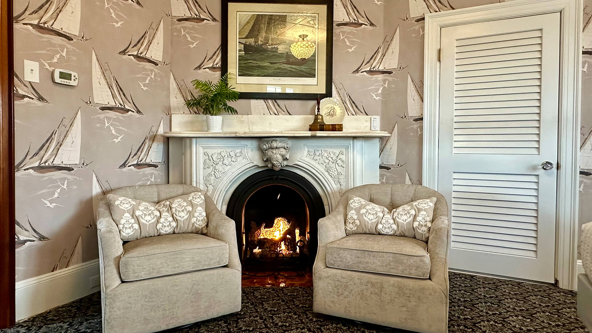 A cozy seating area with a fireplace, two armchairs, and a framed picture above the mantel.
