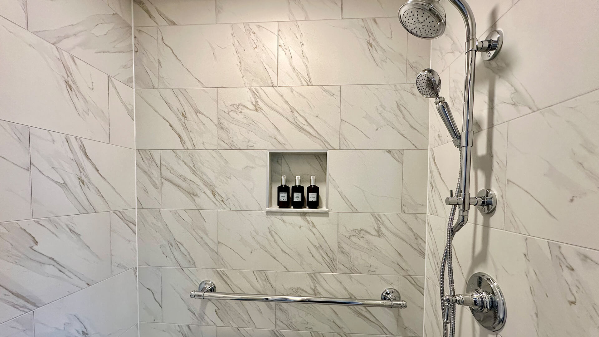 A shower with marble tiles, a shower head, and soap bottles.