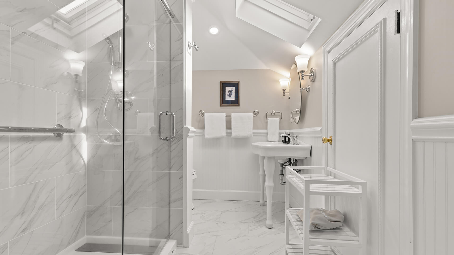 A clean and well-lit bathroom with a glass-enclosed shower, marble tiles, and a sink area.
