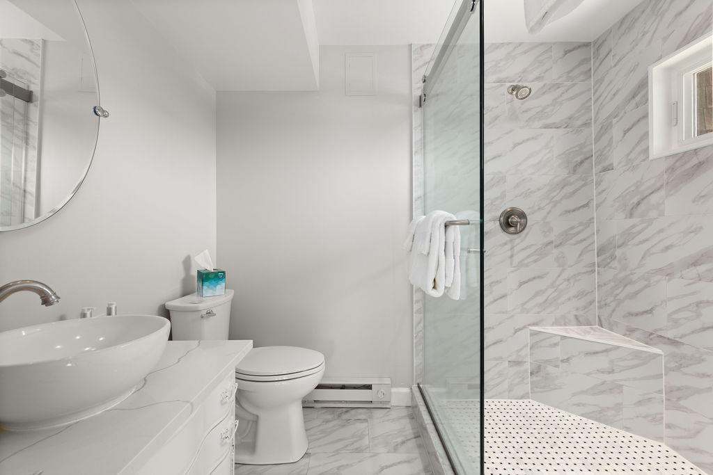A modern bathroom with marble tiles, a glass shower door, and a white sink.