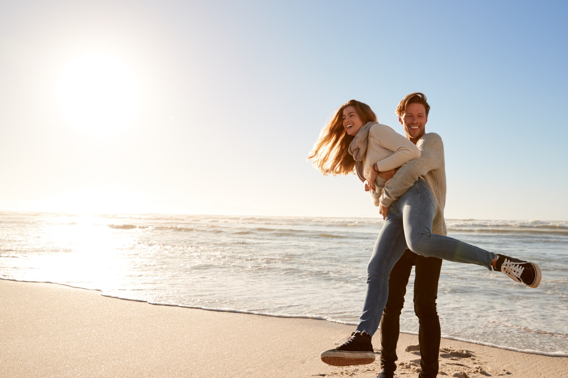 A man carrying a woman on his back on a beach.