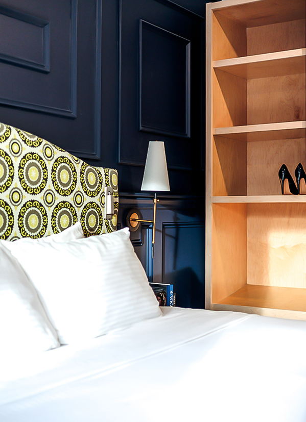 a bed with white sheets and a lamp next to a shelf