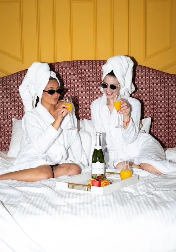 two women wearing white bathrobes and towels on their heads sitting on a bed