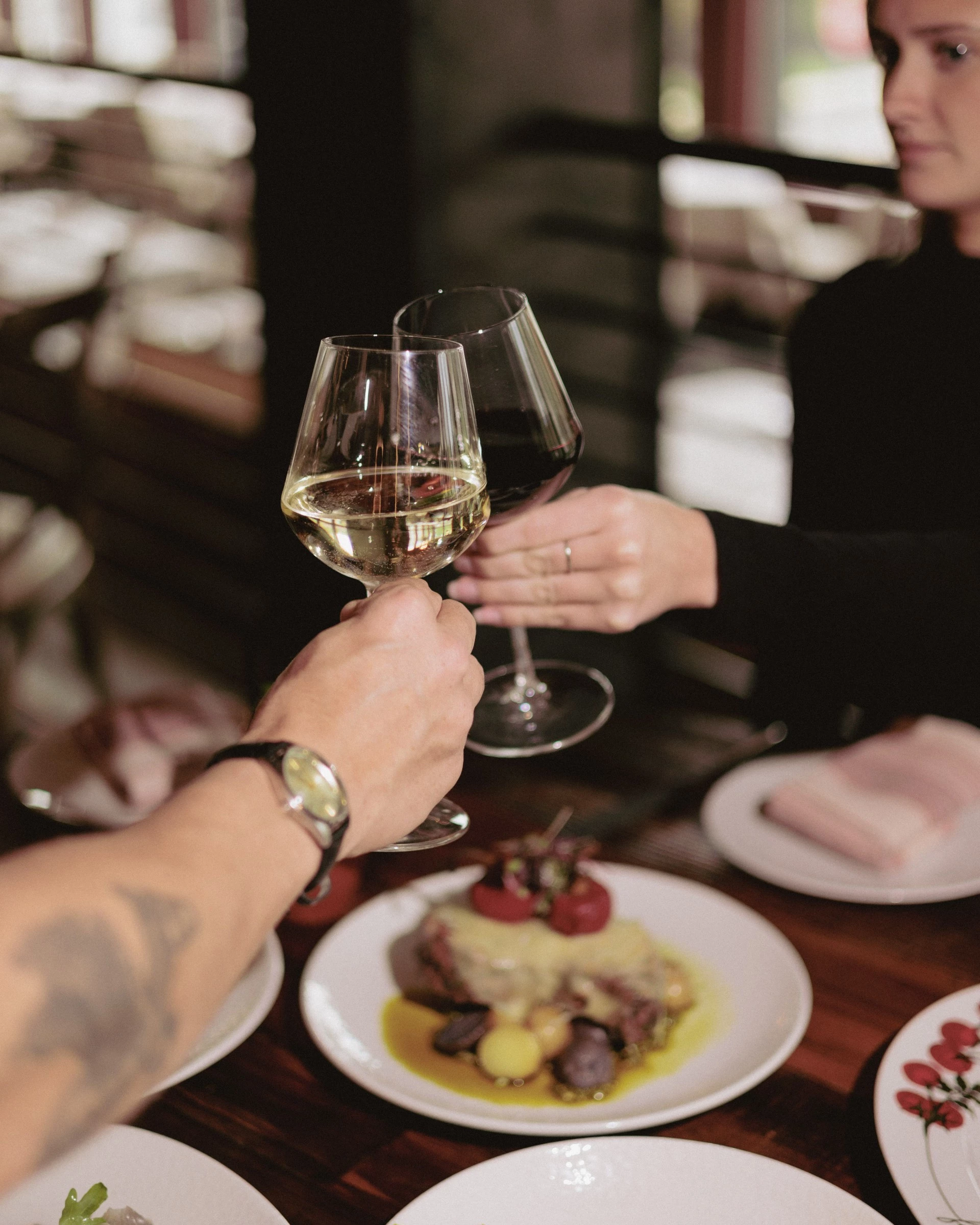 a person holding wine glasses with food on the table
