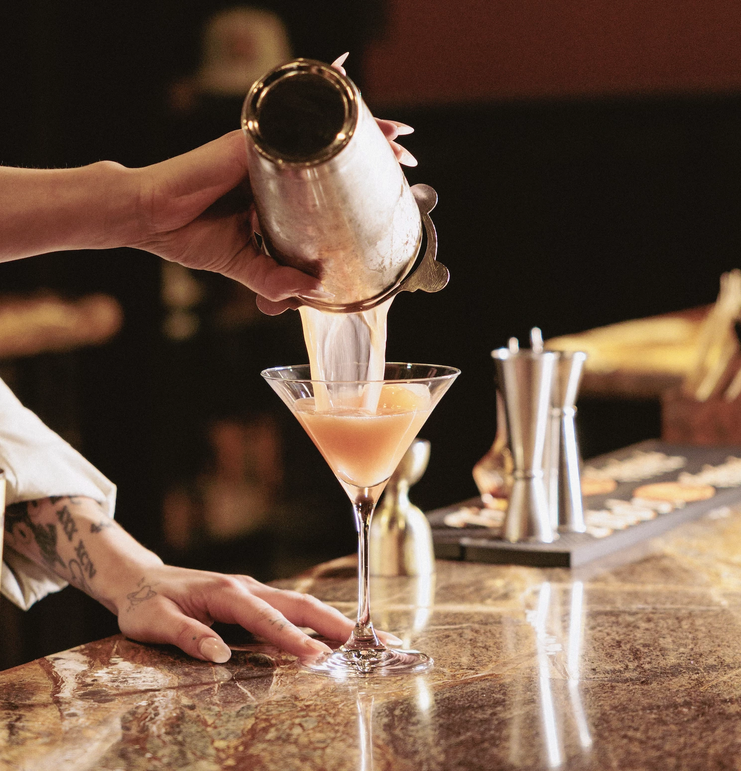 a person pouring a drink into a martini glass