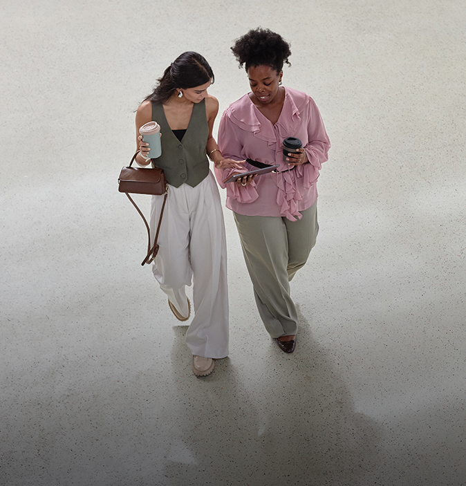a woman walking with another woman holding a tablet