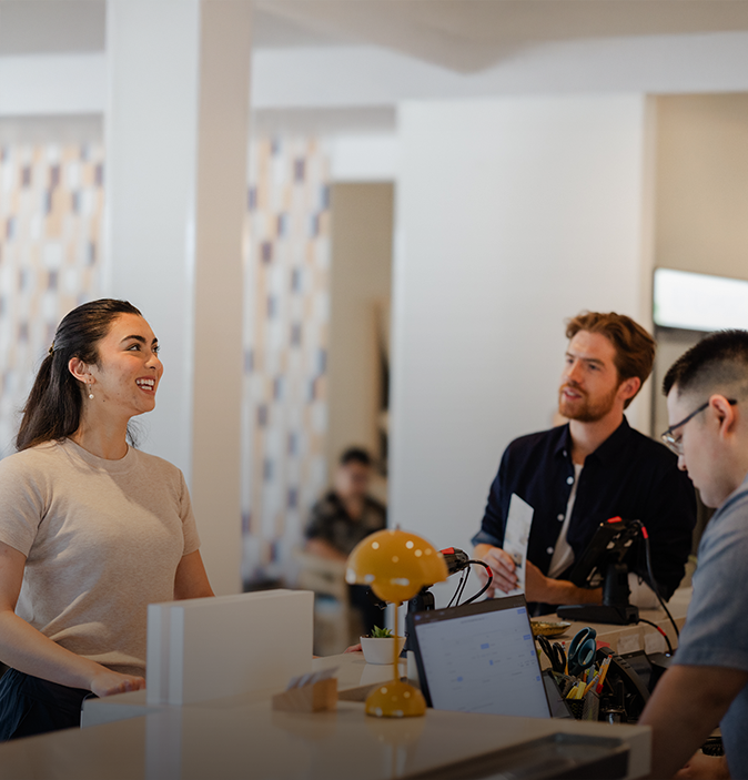 a woman smiling at a desk with a man behind her