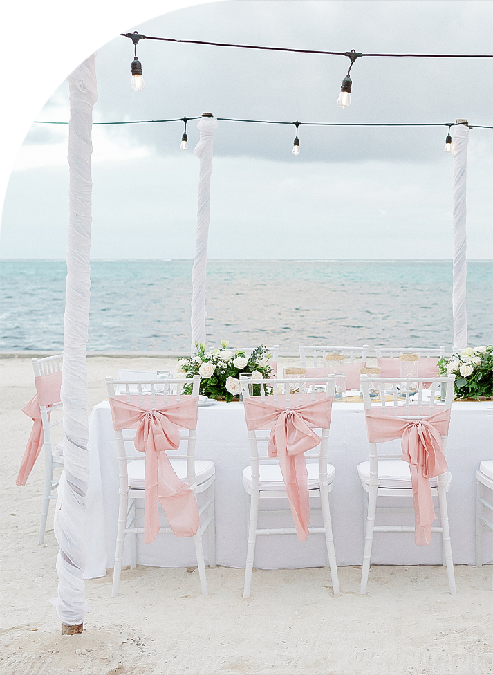 a table set up with chairs and flowers on the beach