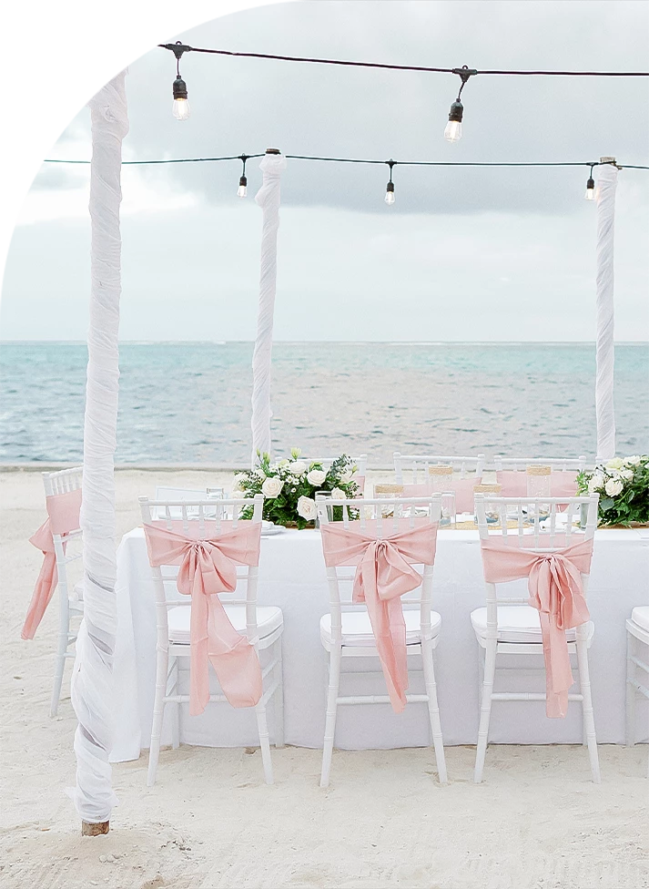 a table set up with chairs and flowers on the beach