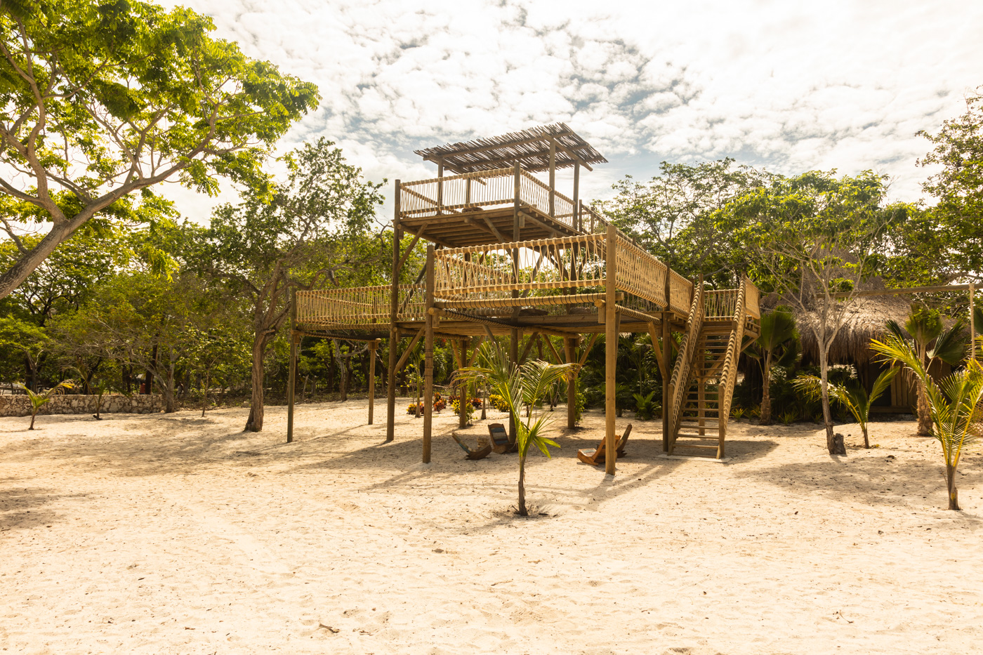 a wooden structure with a deck and a swing in the middle of a sandy area