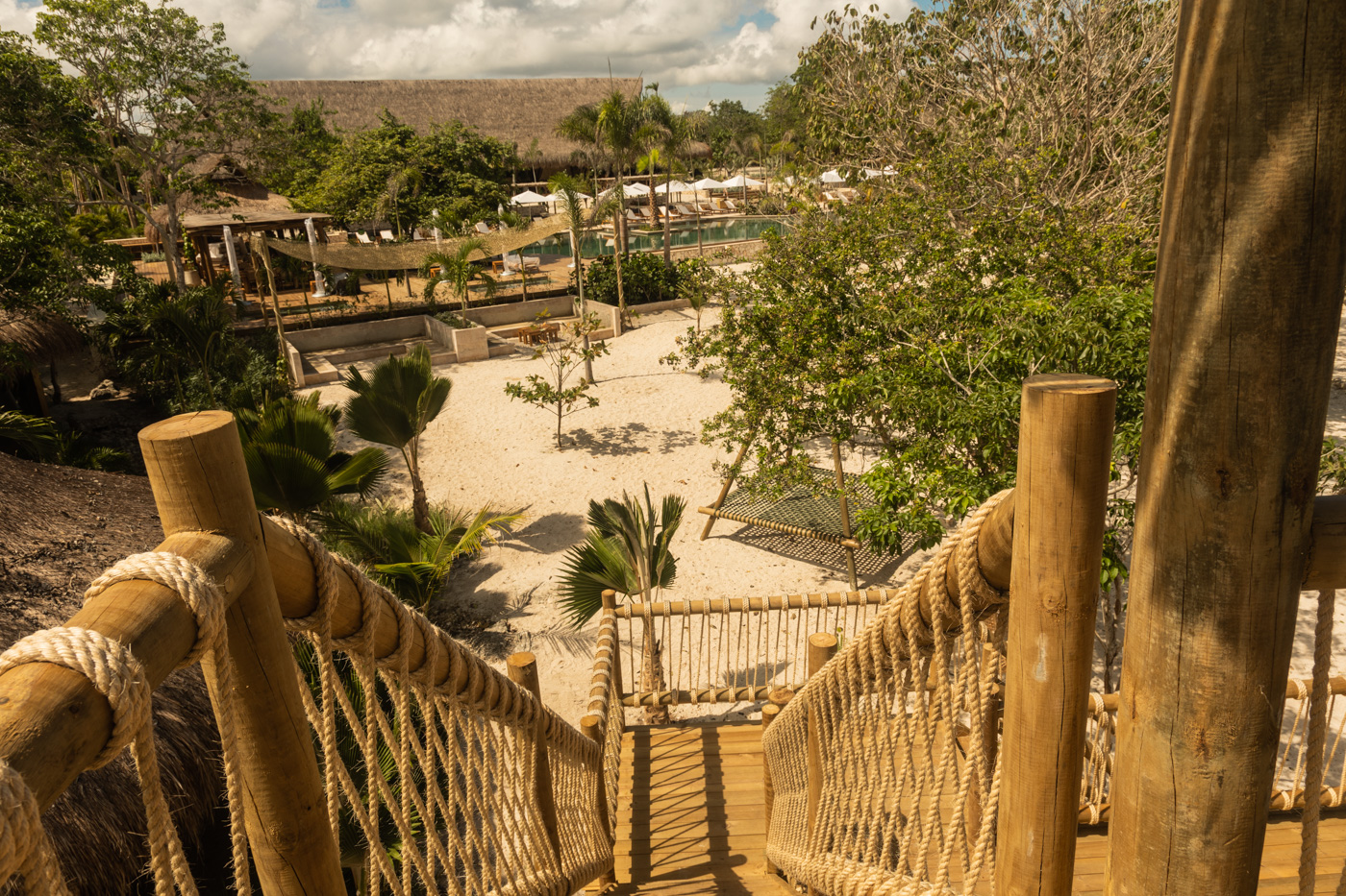 a wooden bridge with rope railings and trees and a pool