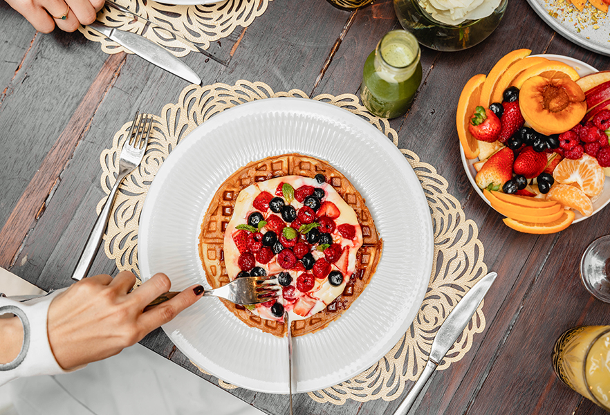 a person eating a waffle with fruit on a plate