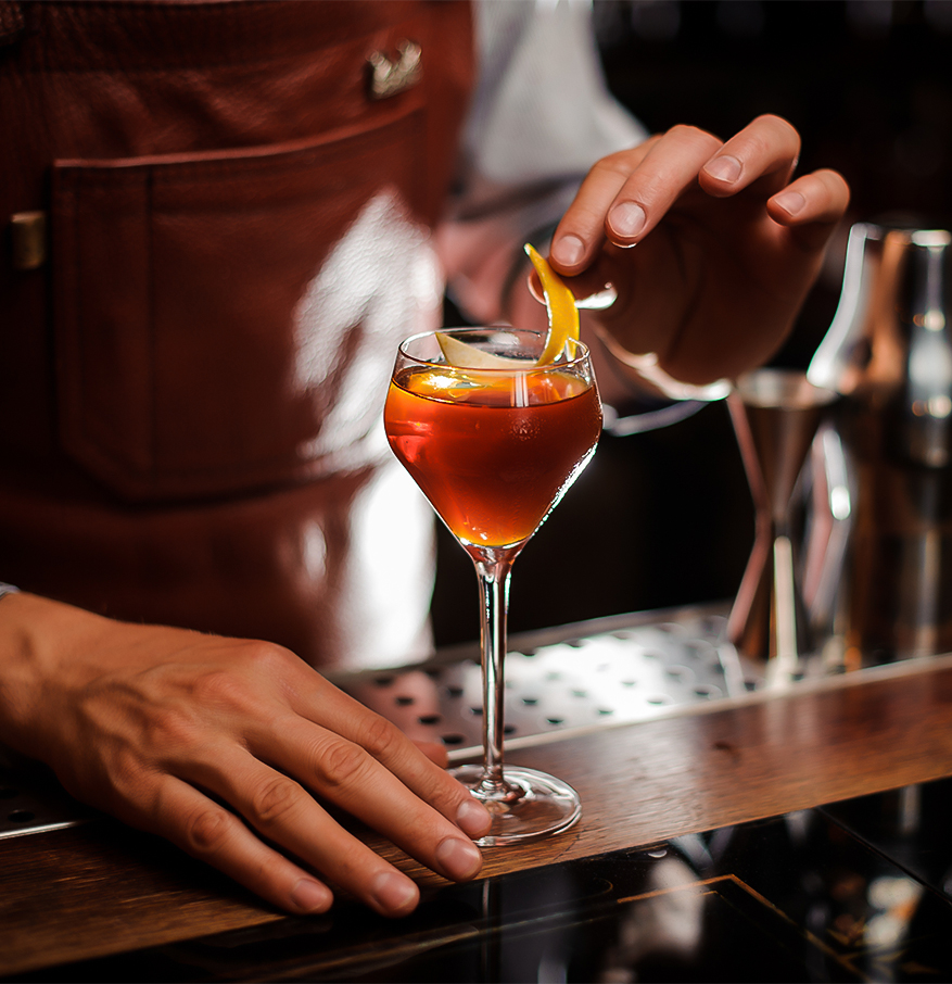 a person putting a slice of orange into a glass of alcohol
