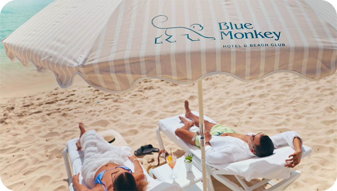 a couple of people lying on lounge chairs under an umbrella on a beach