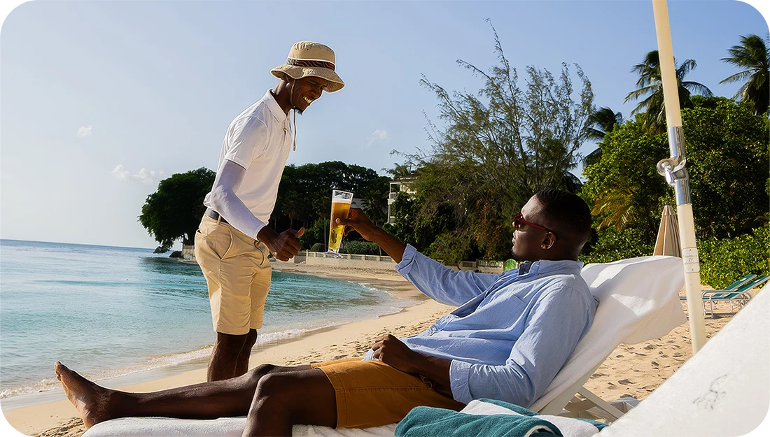 a man giving a drink to another man on a beach
