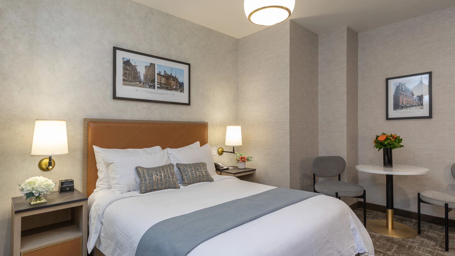 A hotel room with a bed, nightstands, lamps, a chair, and a small table.