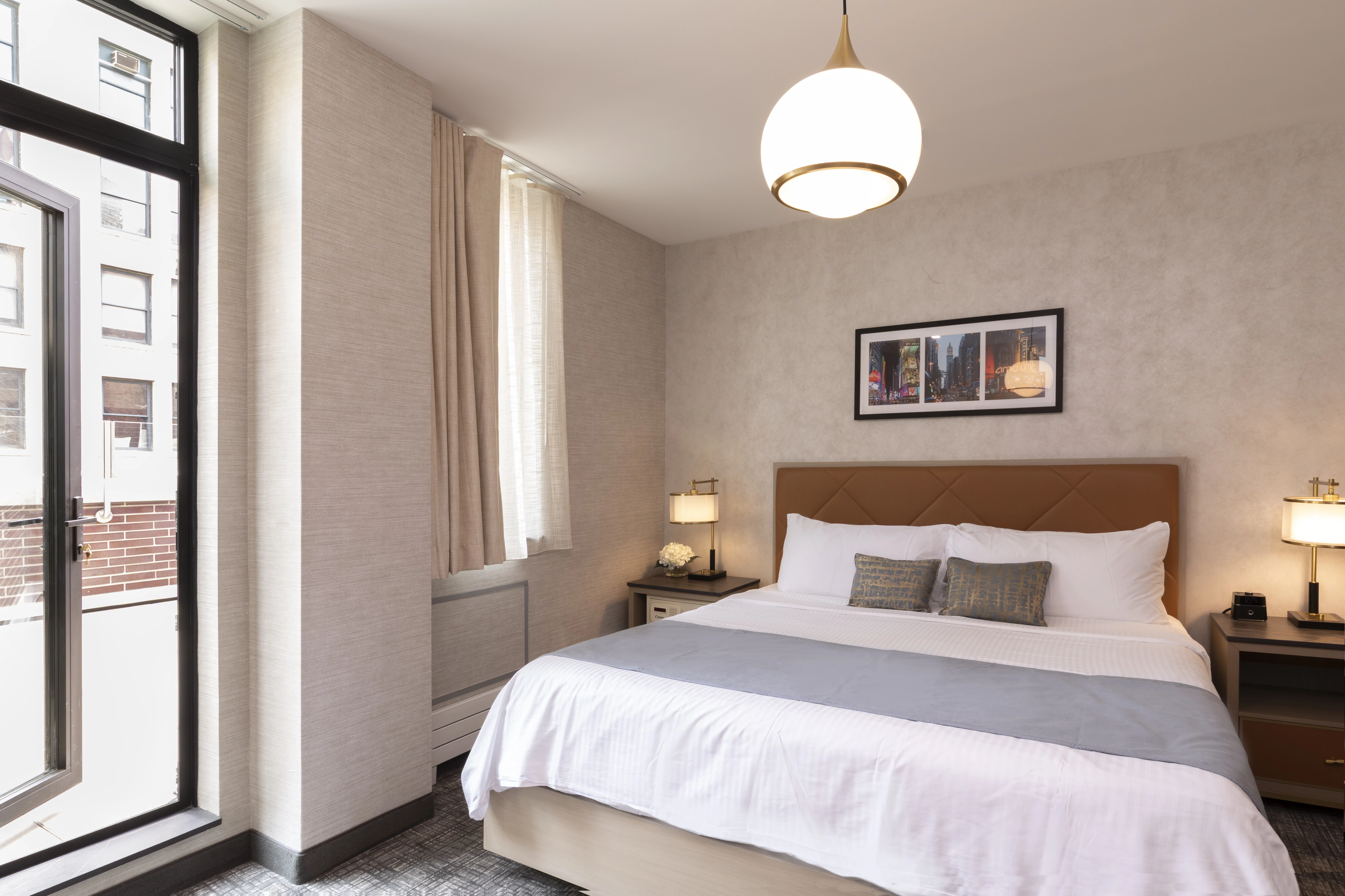 A hotel room with a bed, nightstands, lamps, and a window showing a city view.