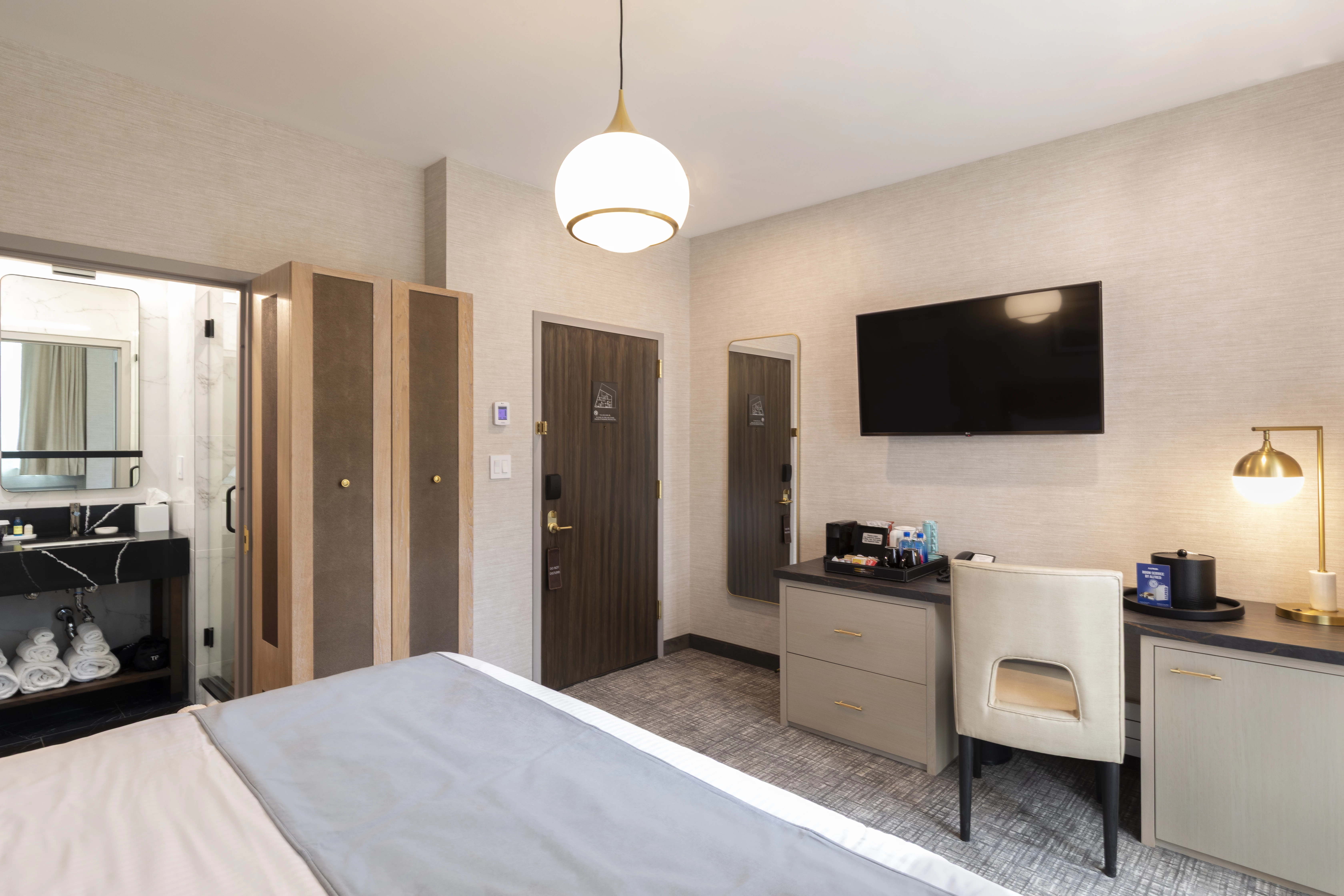 A wide view of a hotel room with a bed, desk, TV, and chair