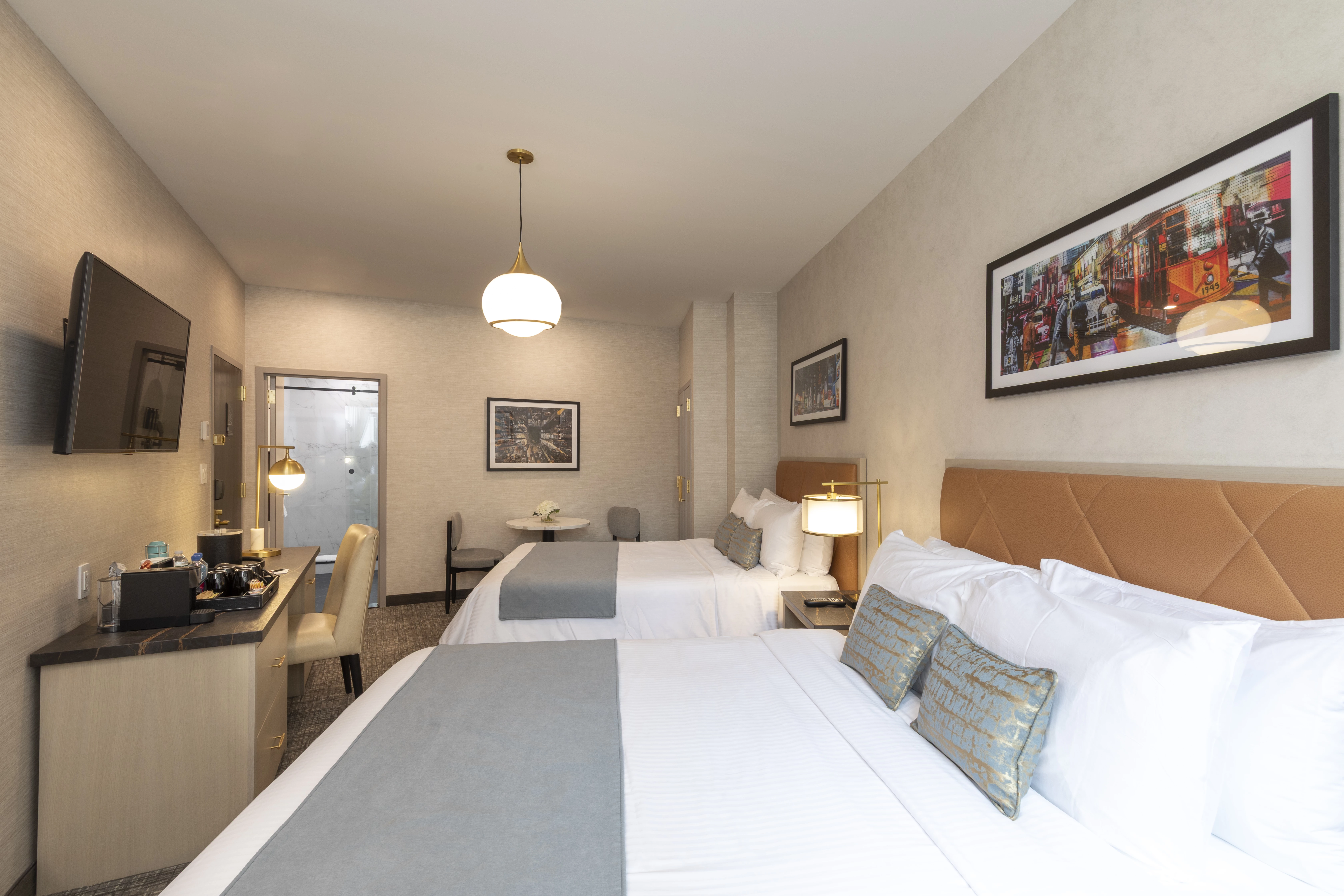 A hotel room with a large bed, desk, TV, and artwork