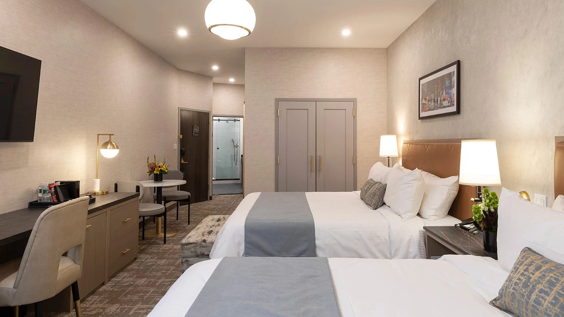 A hotel room with two beds, a desk, TV, and shower
