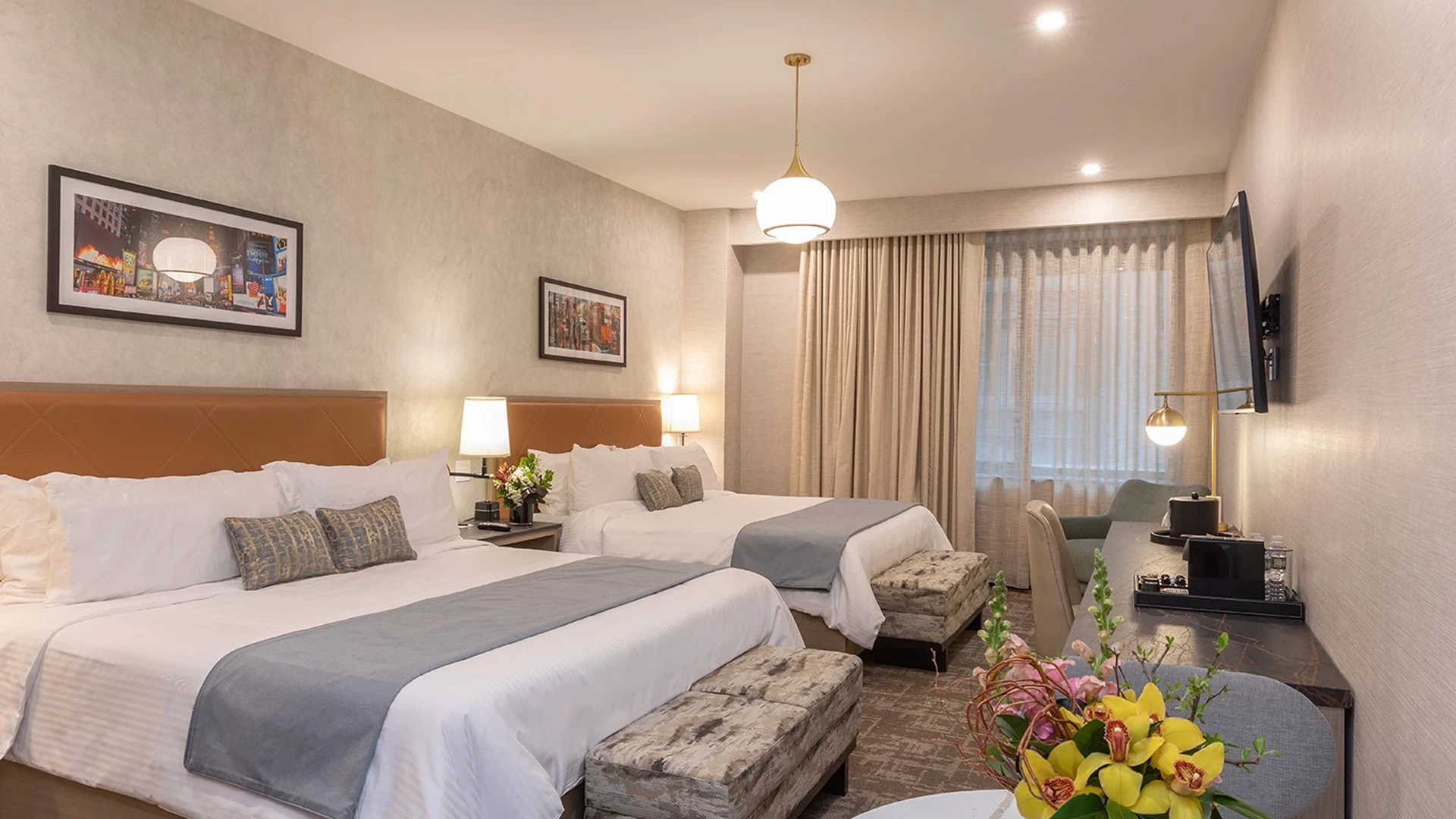 A hotel room with two beds, a desk, and a TV