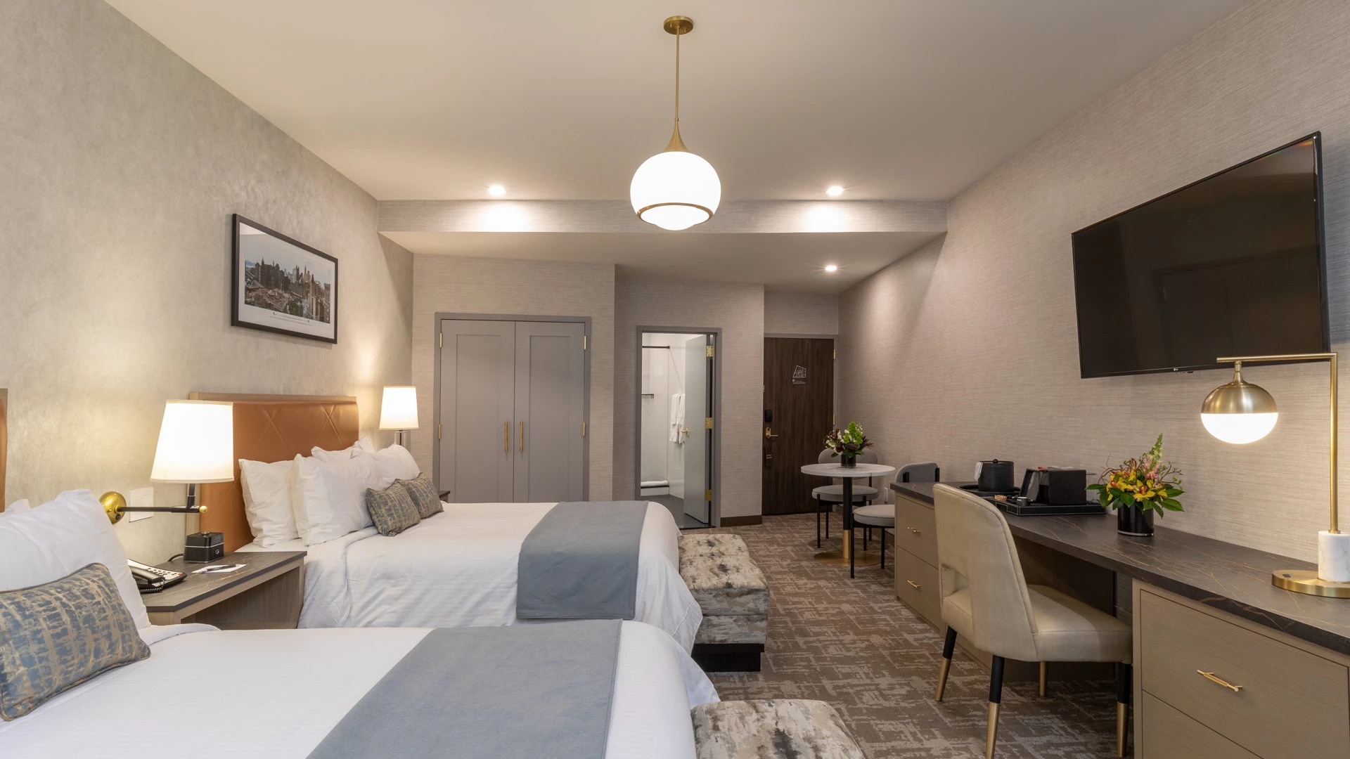A hotel room with two beds, a desk, and a TV