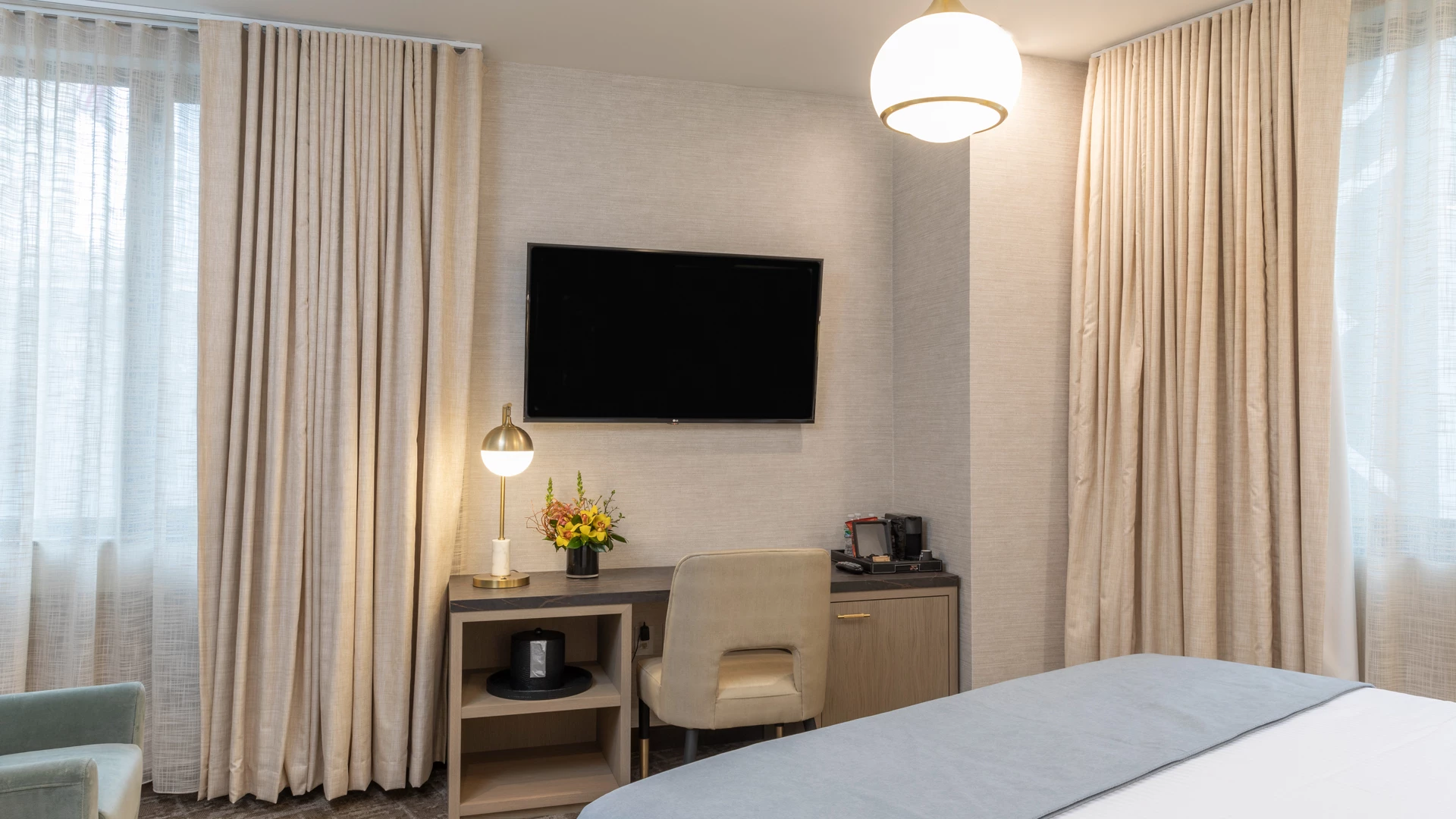 A hotel room with a desk, TV, bed, and chair