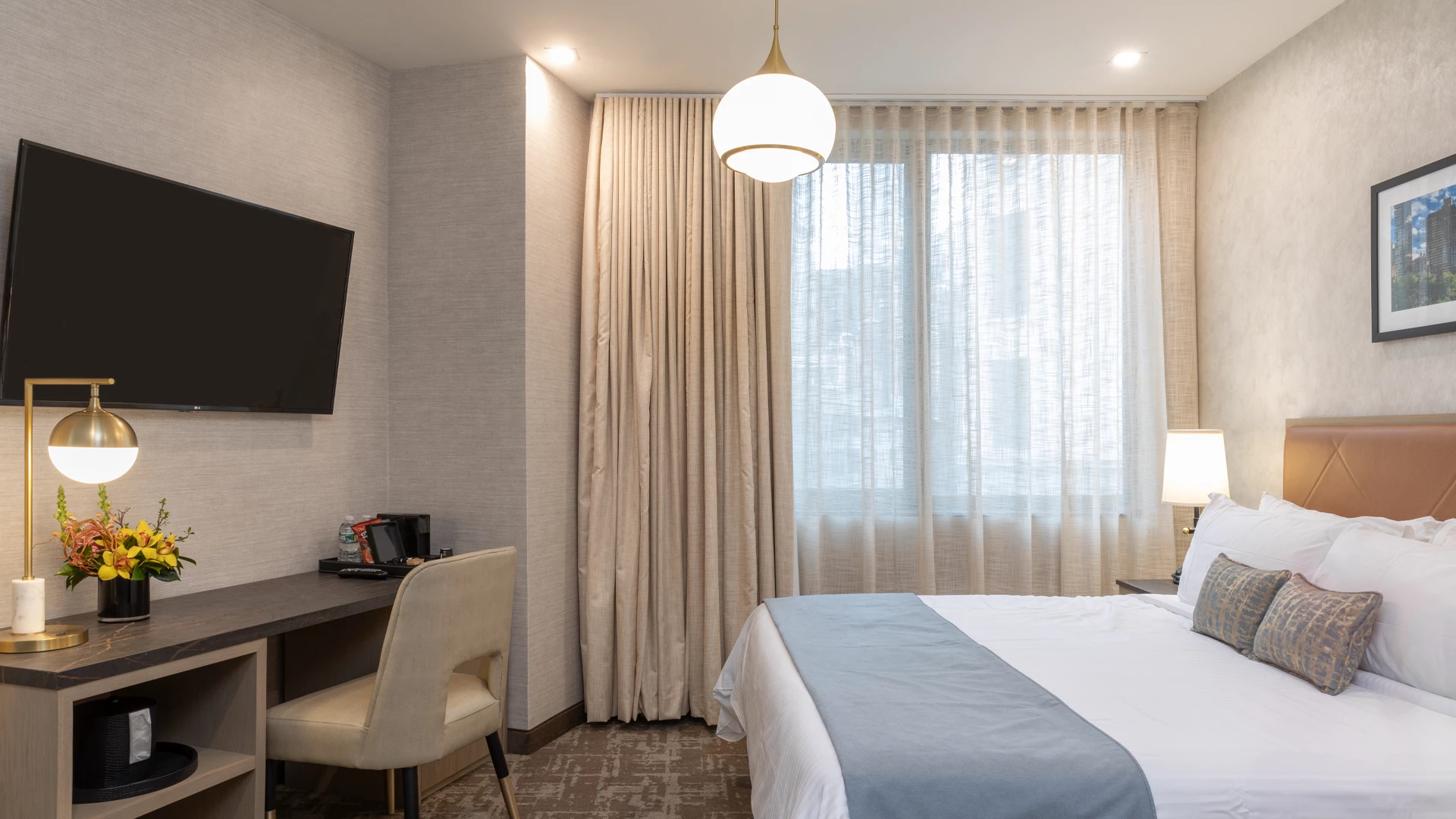 A hotel room with a bed, desk, TV, and window