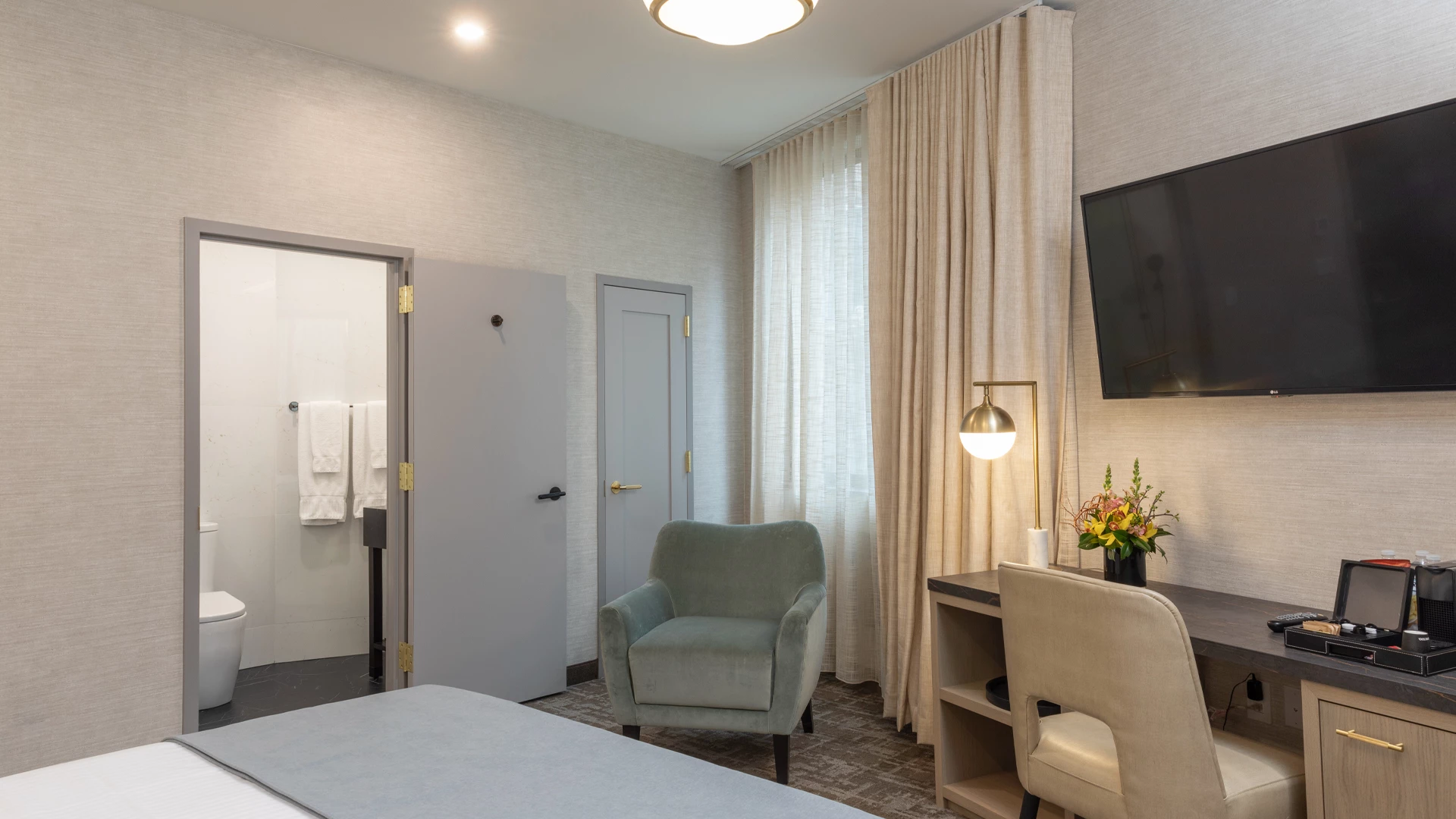 A hotel room with a bed, desk, chair, and TV on the wall.