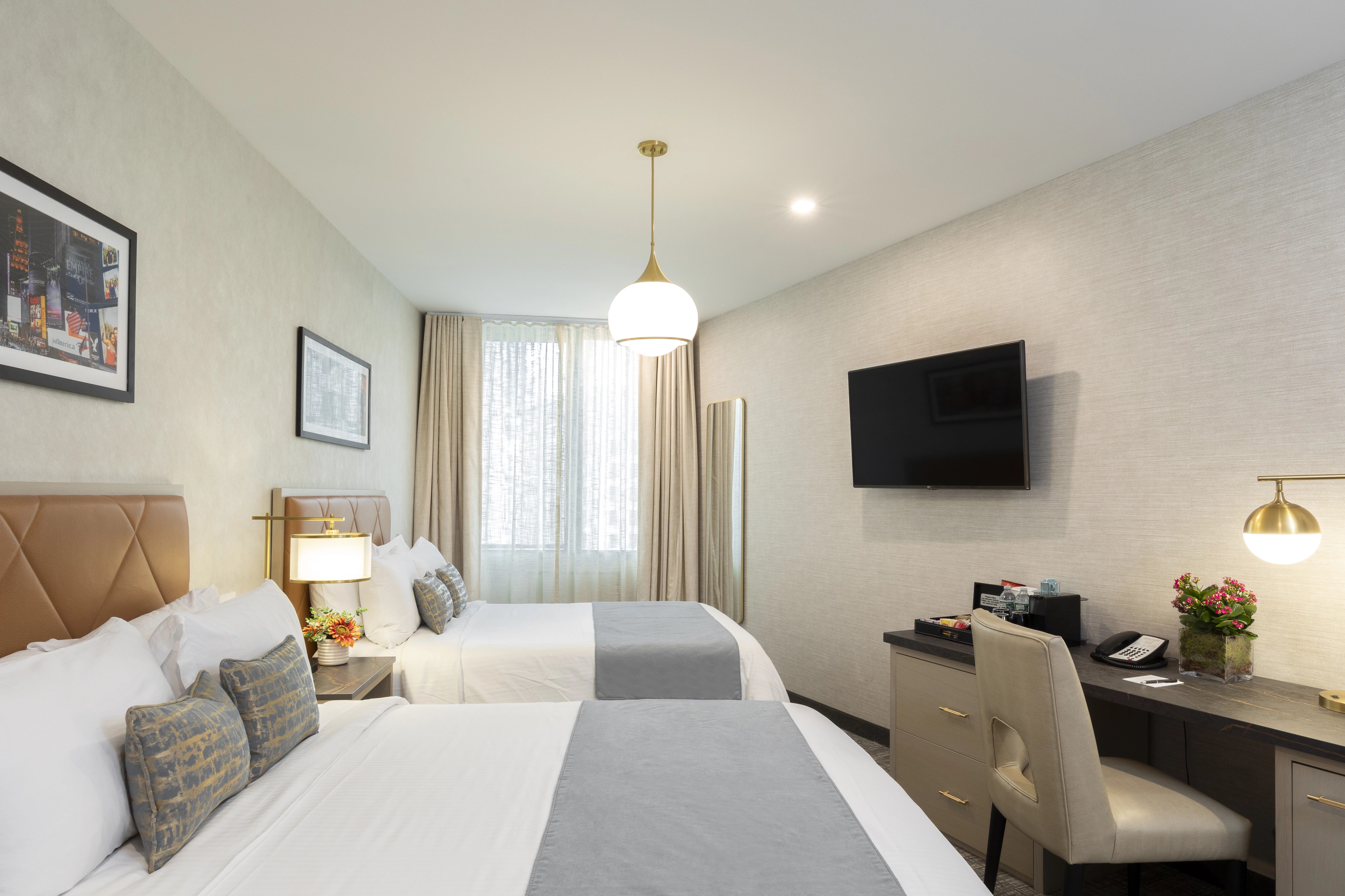 A hotel room with two beds, a desk, and a TV on the wall.