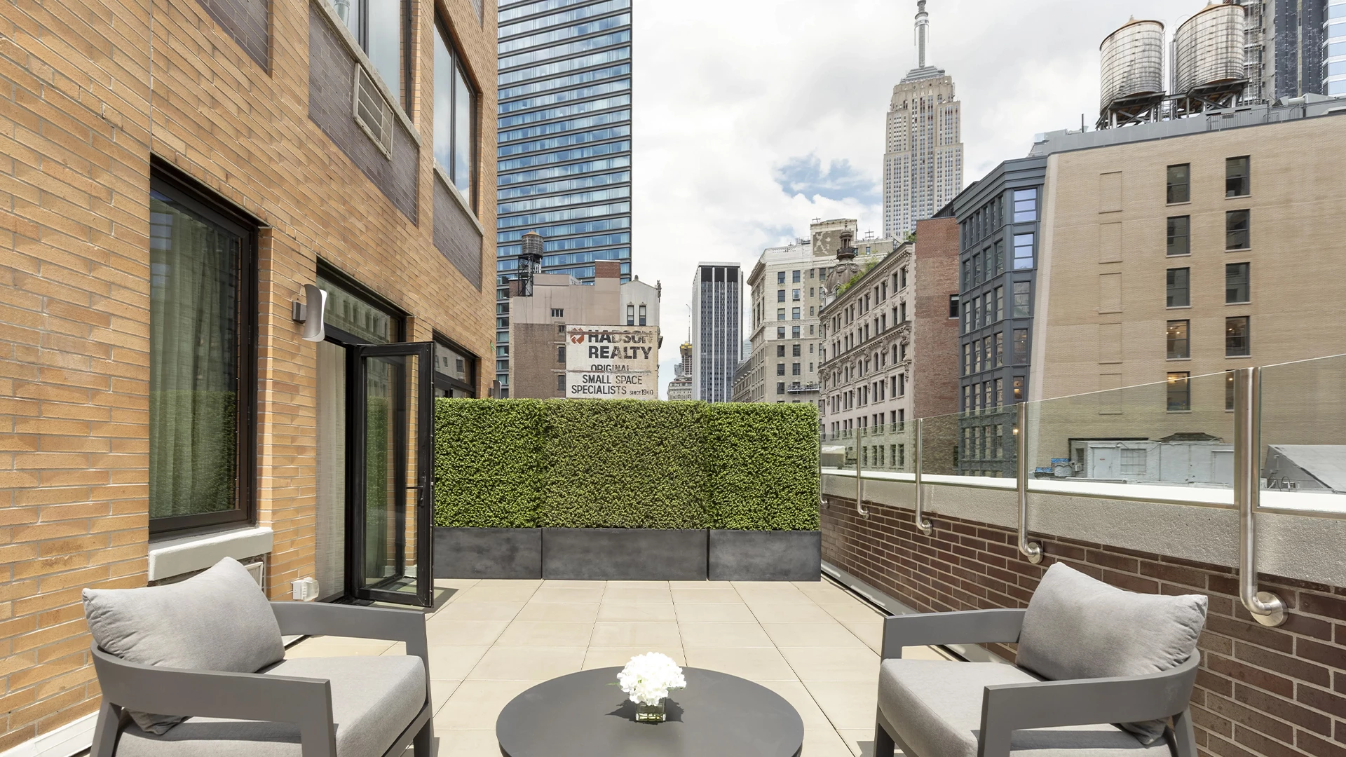 A small outdoor seating area with two chairs and a table on a balcony overlooking the city.
