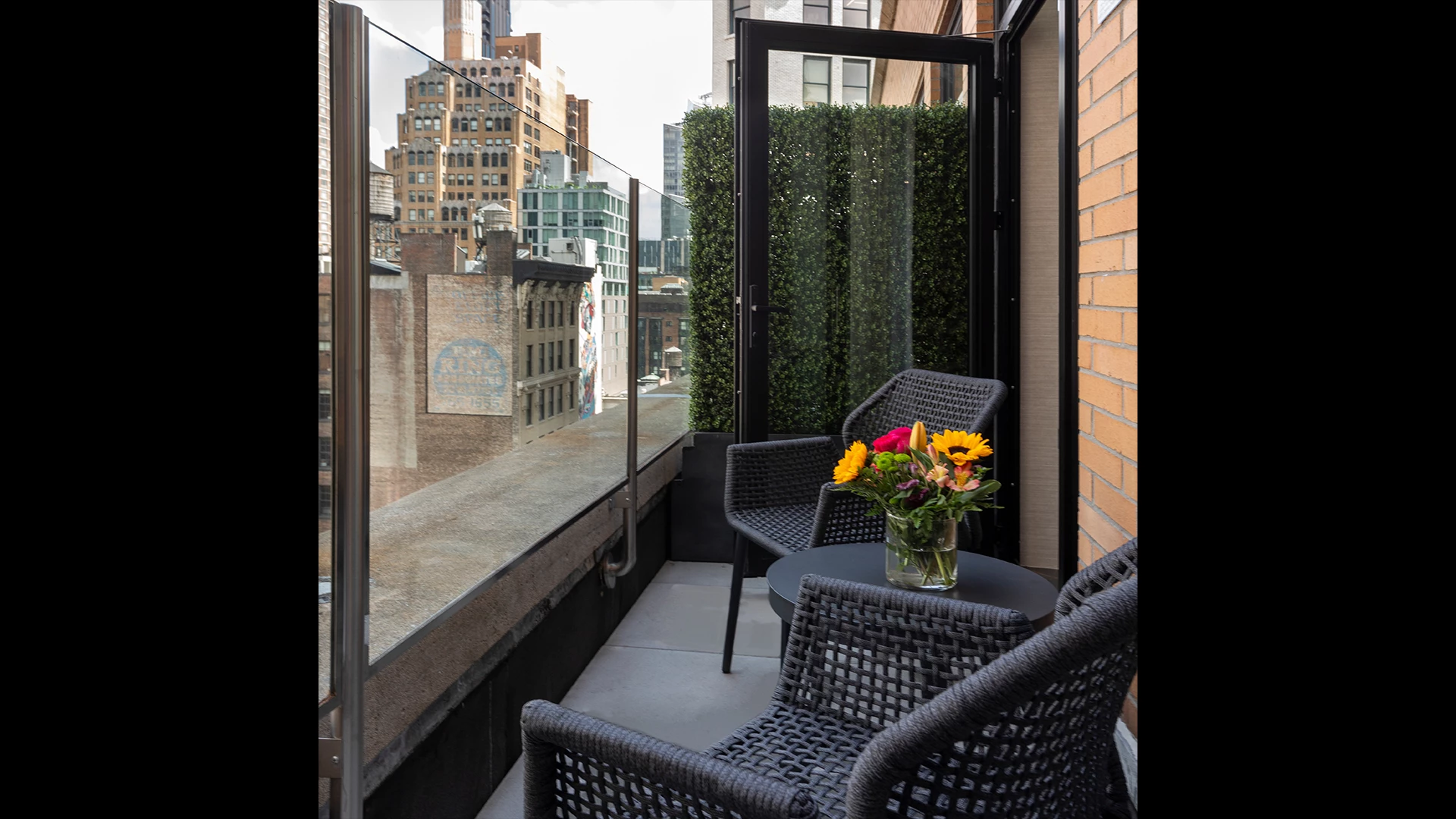 A balcony with a table and chairs, flowers, and a city view