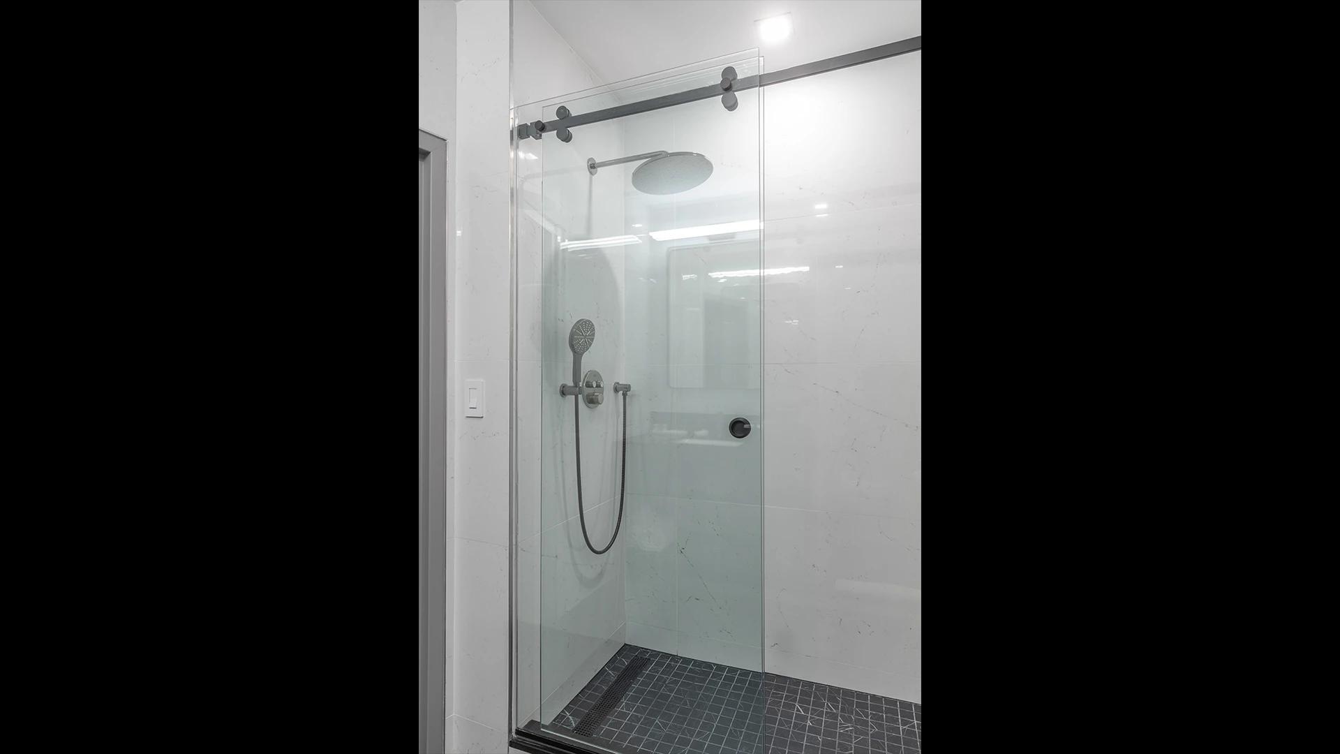A modern bathroom shower with a glass door, marble walls, and a black tile floor.