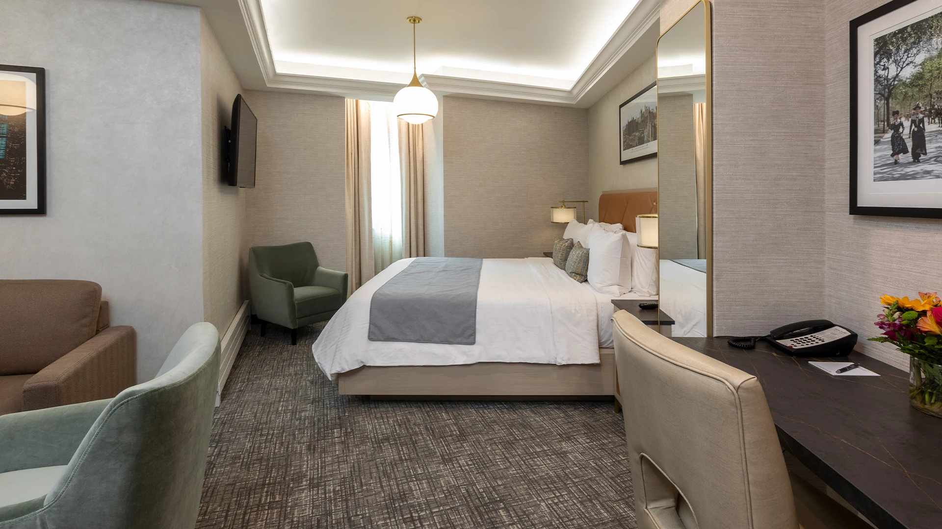 A hotel room with a bed, desk, chair, sofa, TV, and mirror