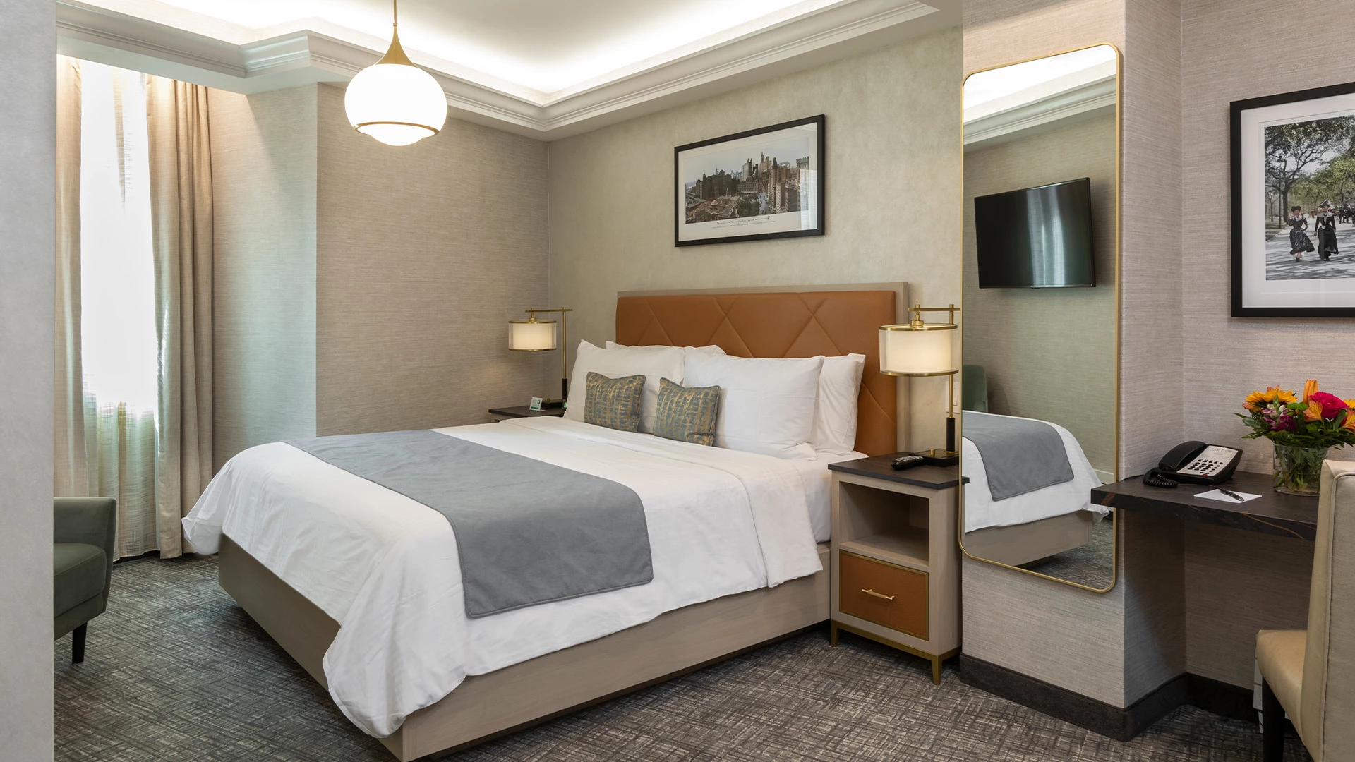 A hotel room with a large bed, nightstand, mirror, desk, and chair.