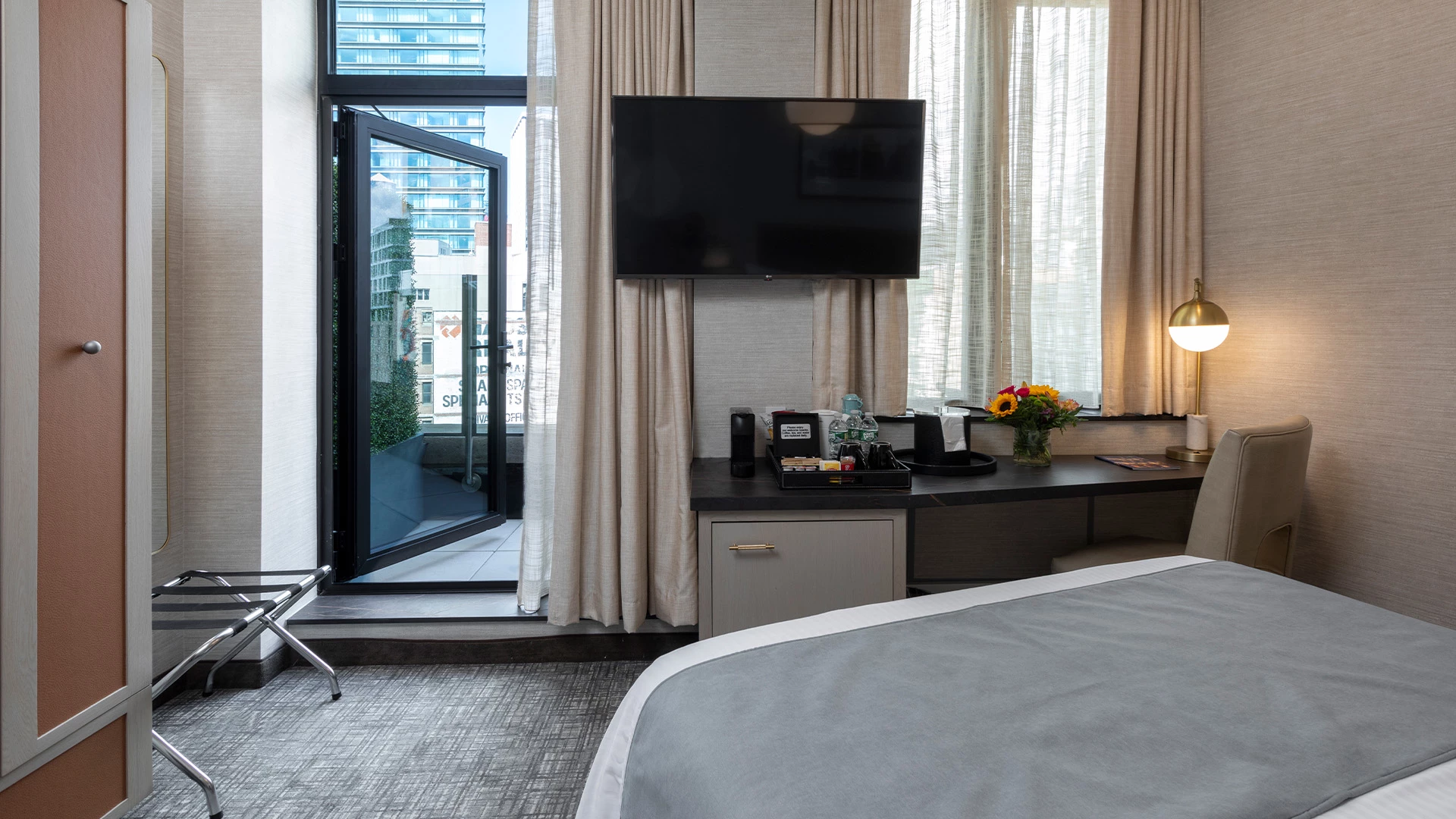 A hotel room with a bed, desk, TV, and balcony