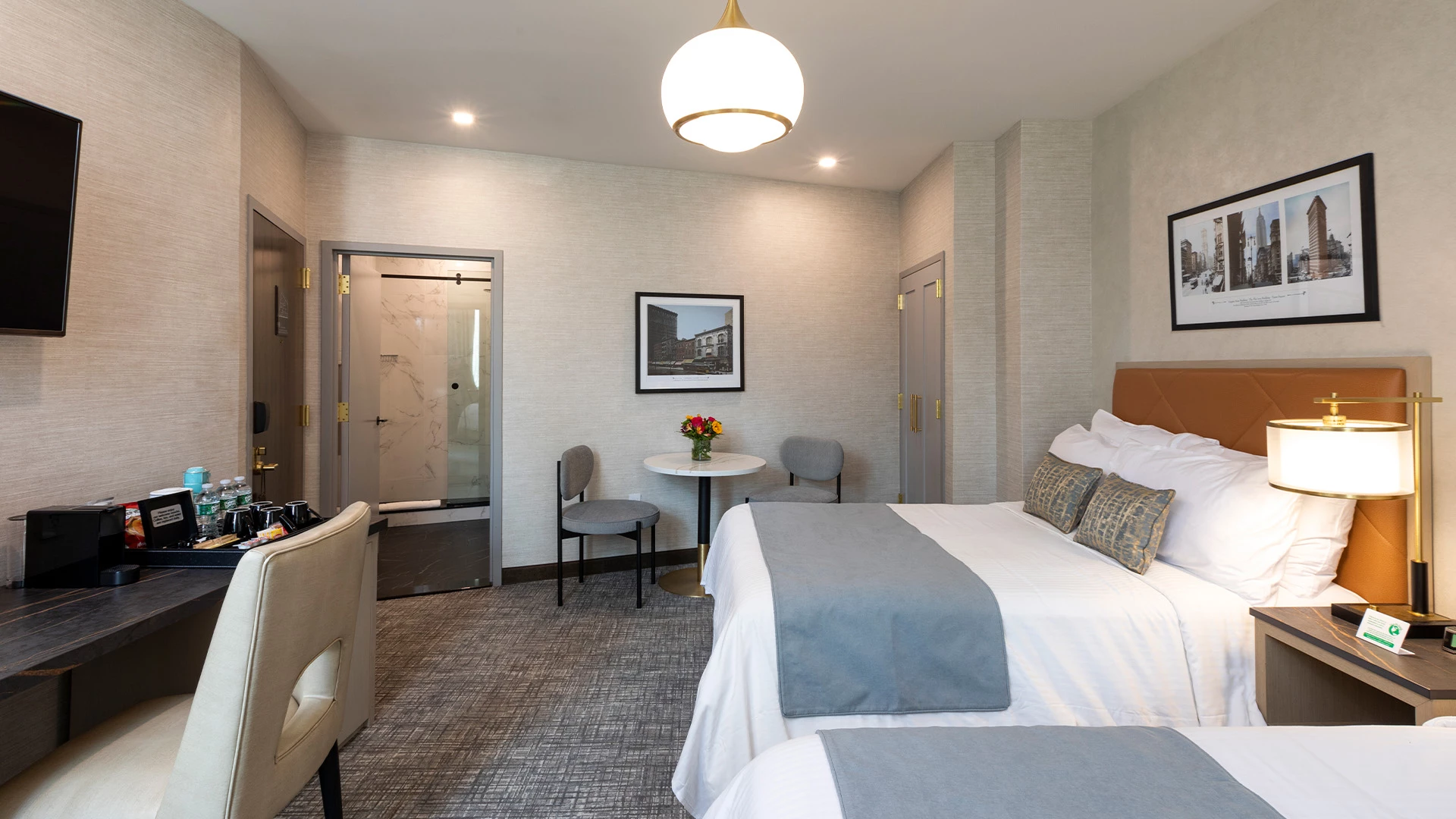 A hotel room with two beds, a desk, and a bathroom in the background.