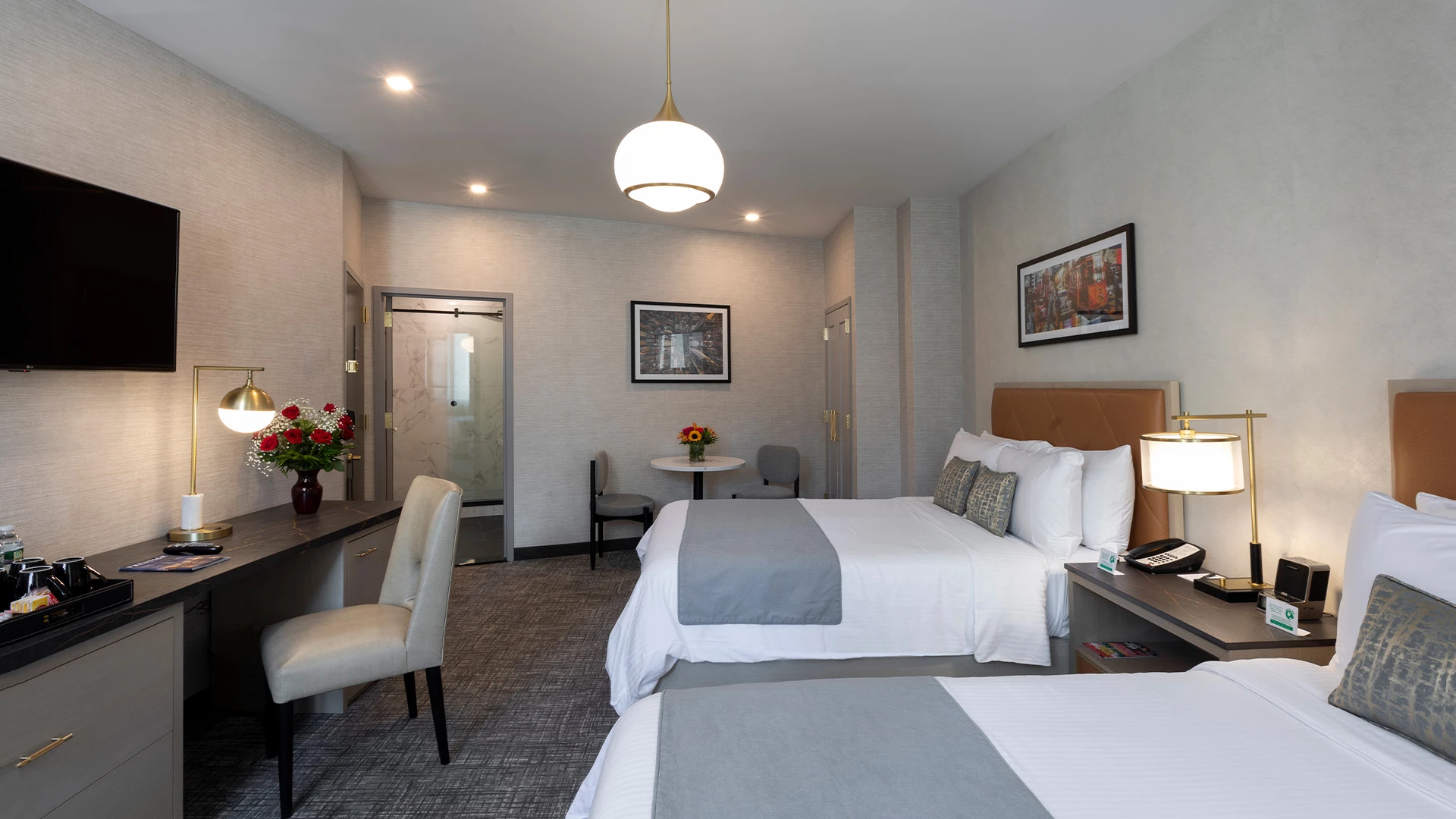 A hotel room with two beds, a desk, TV, and bathroom with shower