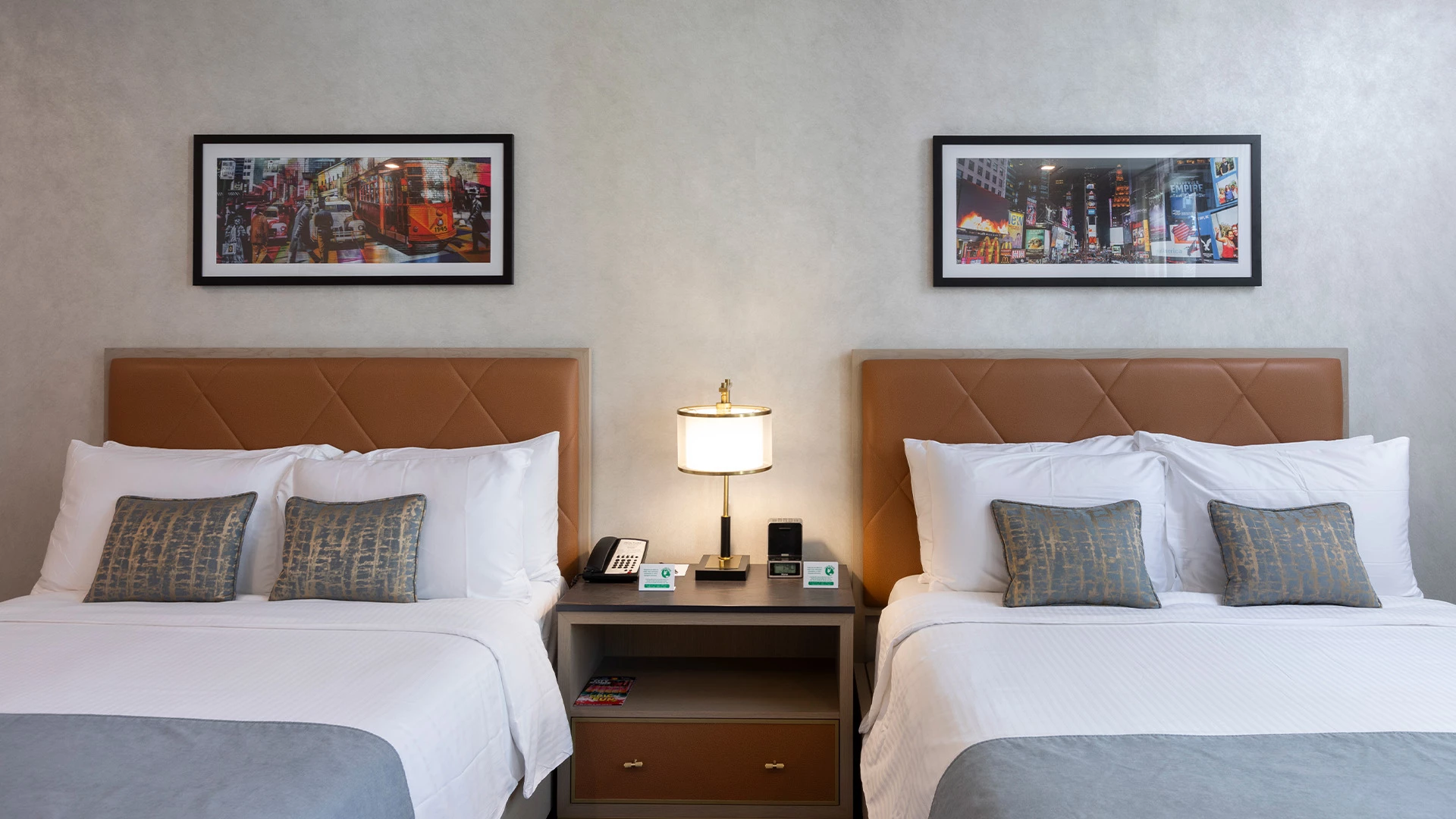 A hotel room with two beds, a nightstand, and artwork on the wall.