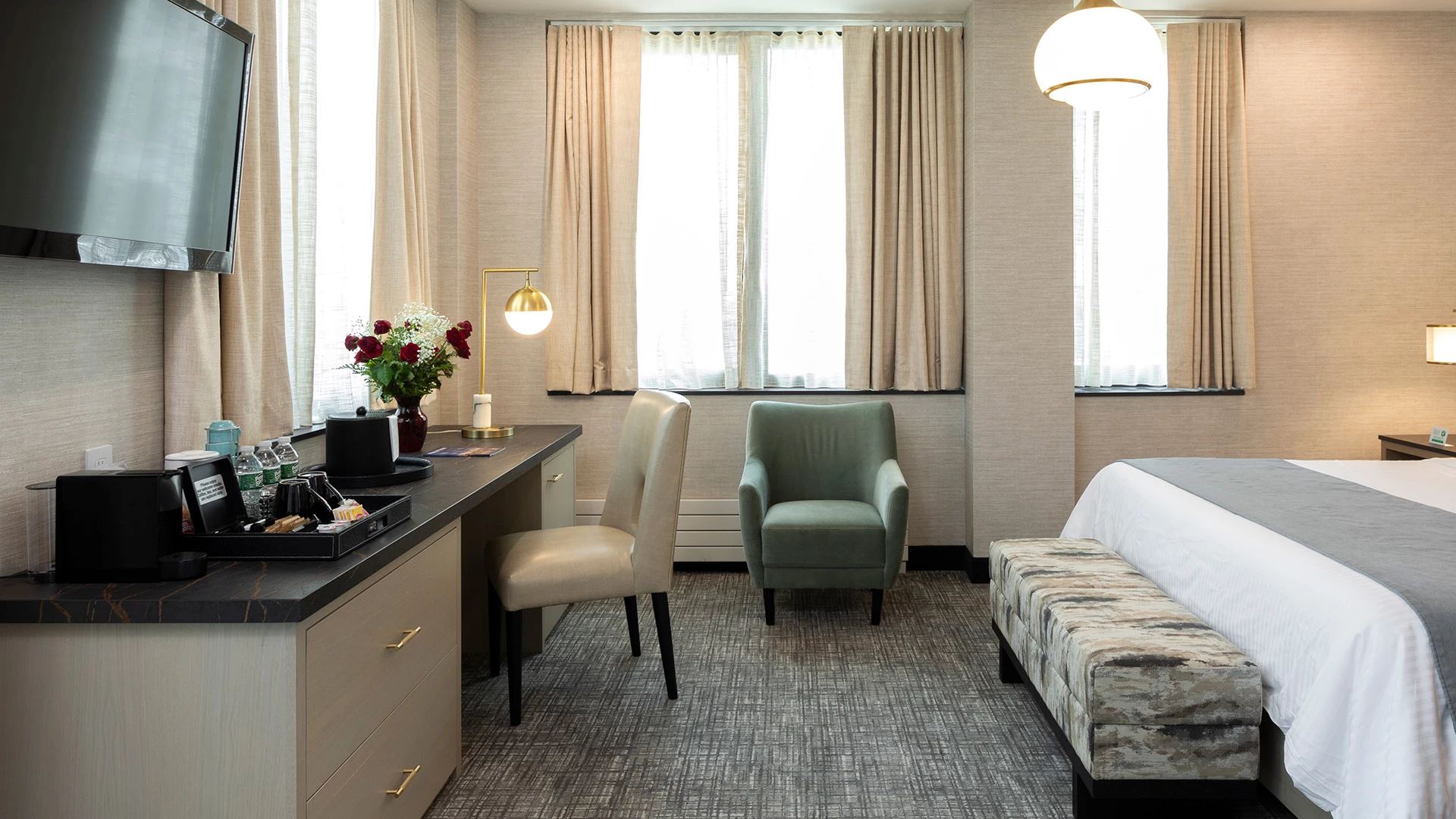A hotel room with a bed, desk, chair, and TV.