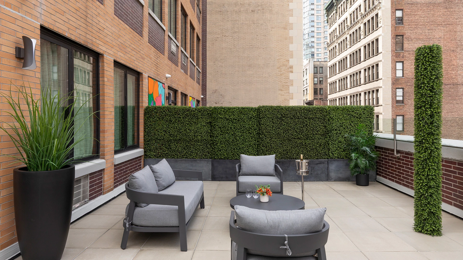 A small outdoor seating area with a hedge, furniture, and a city view