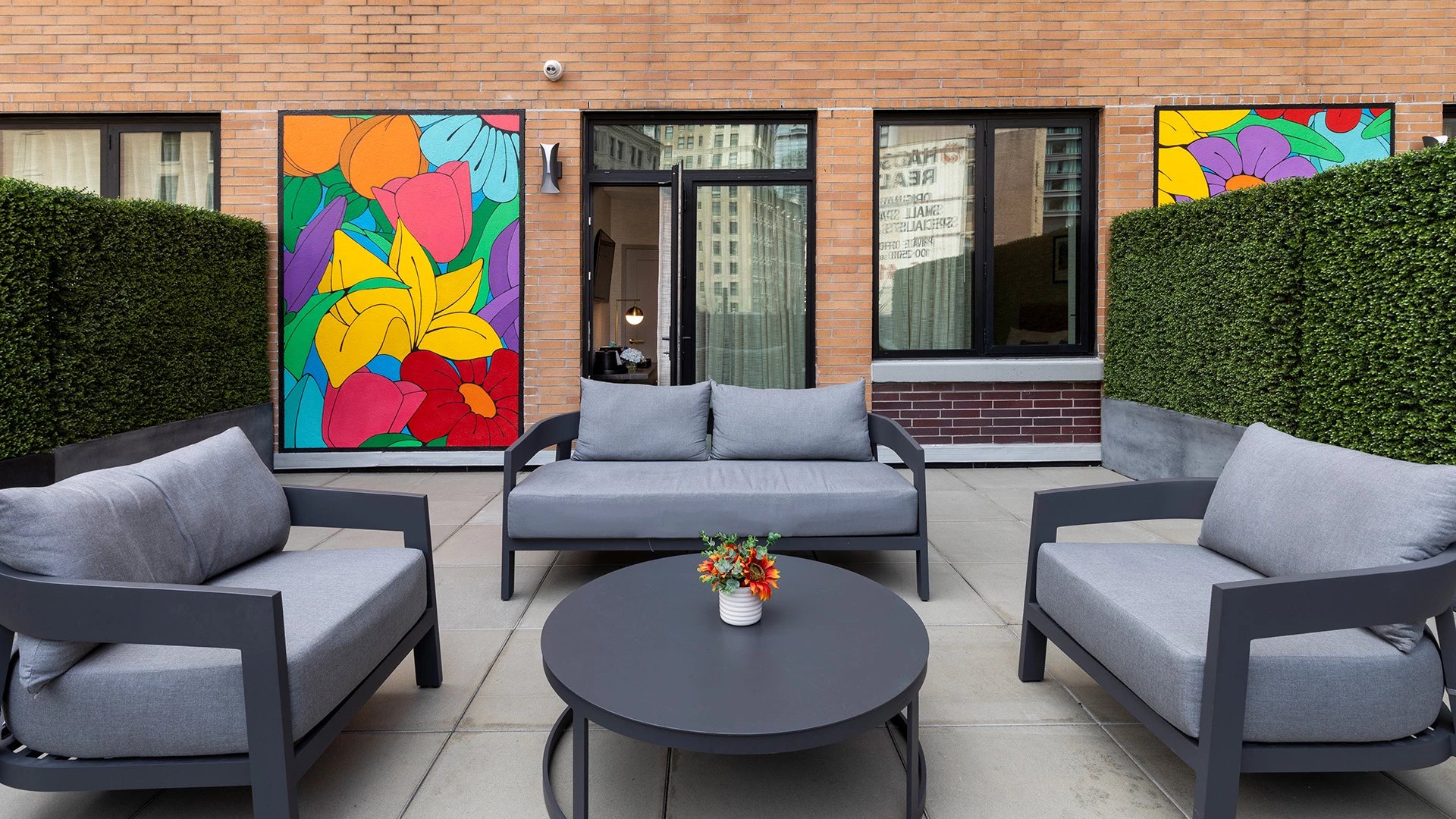 A small outdoor seating area with gray furniture and a vibrant mural on the wall.