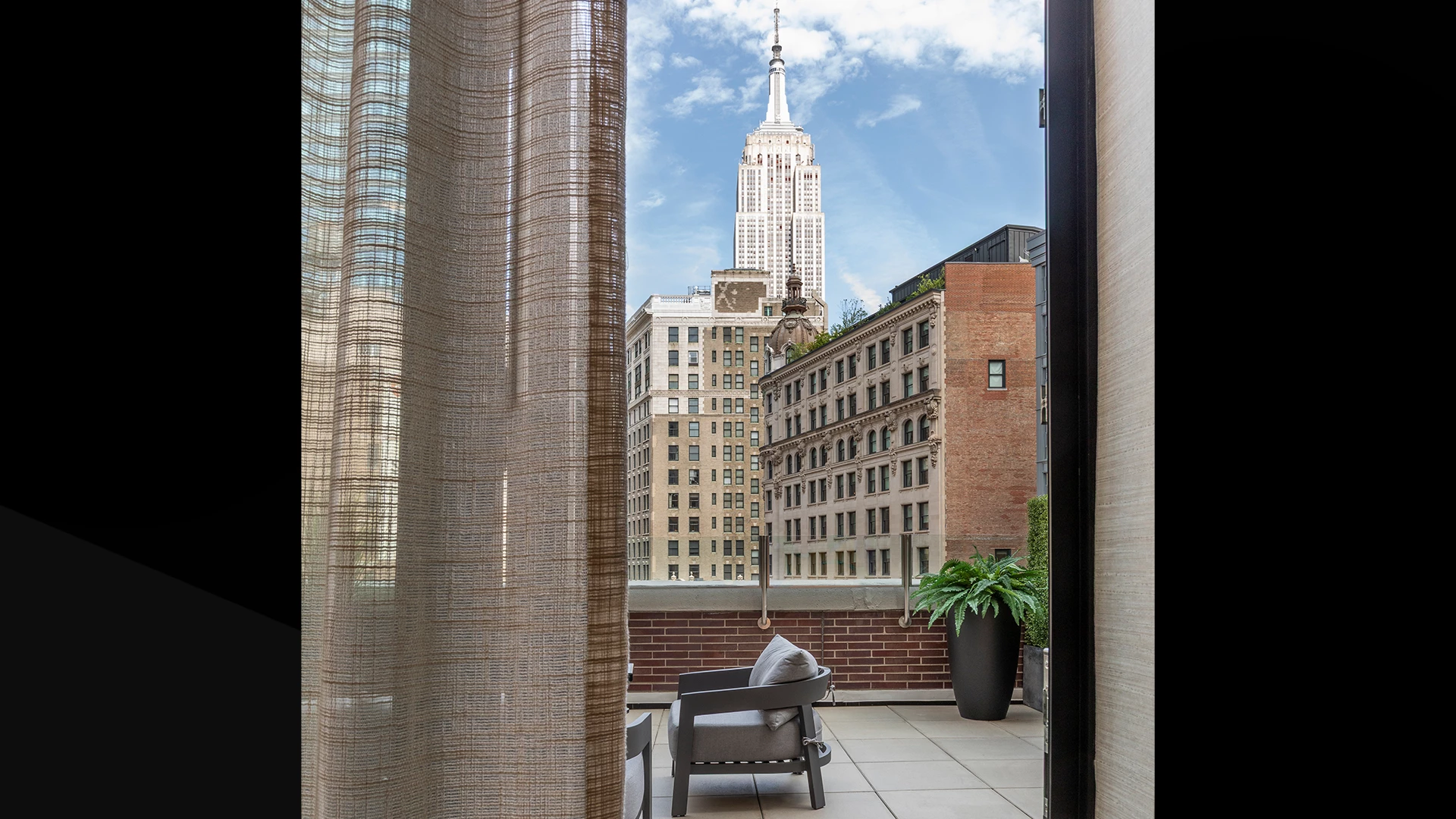 A view of the New York City skyline with the Empire State Building from a balcony with a chair and plant.