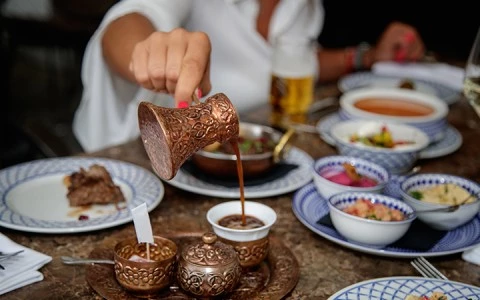 A person pouring coffee into small cups on a table with various dishes.