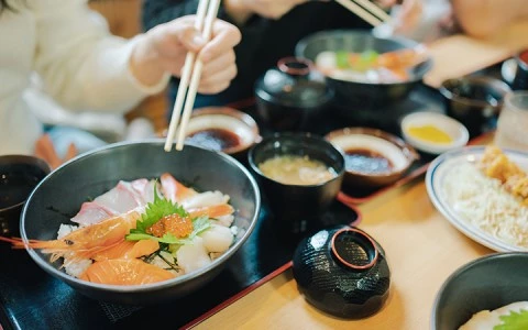 A bowl of sushi with shrimp and other seafood, chopsticks, and a variety of dishes on the table.