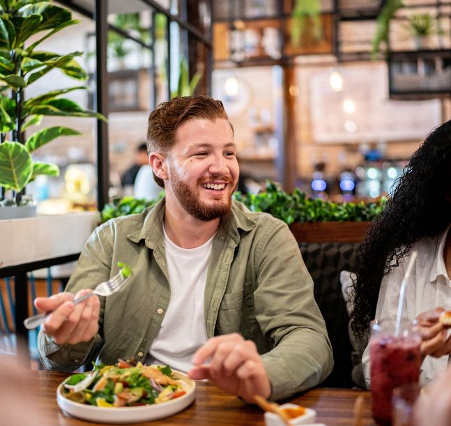 a man smiling at a table with a bowl of salad
