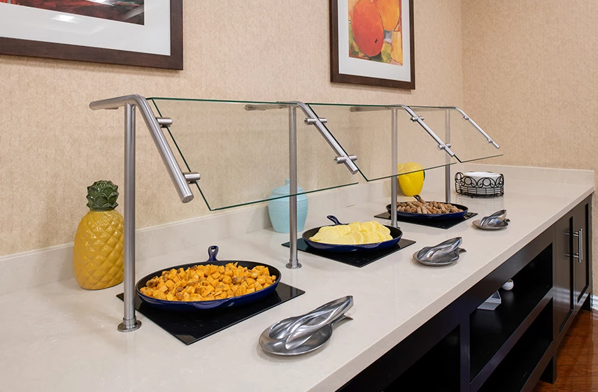 A breakfast buffet with a glass cover, featuring various dishes and fruits.